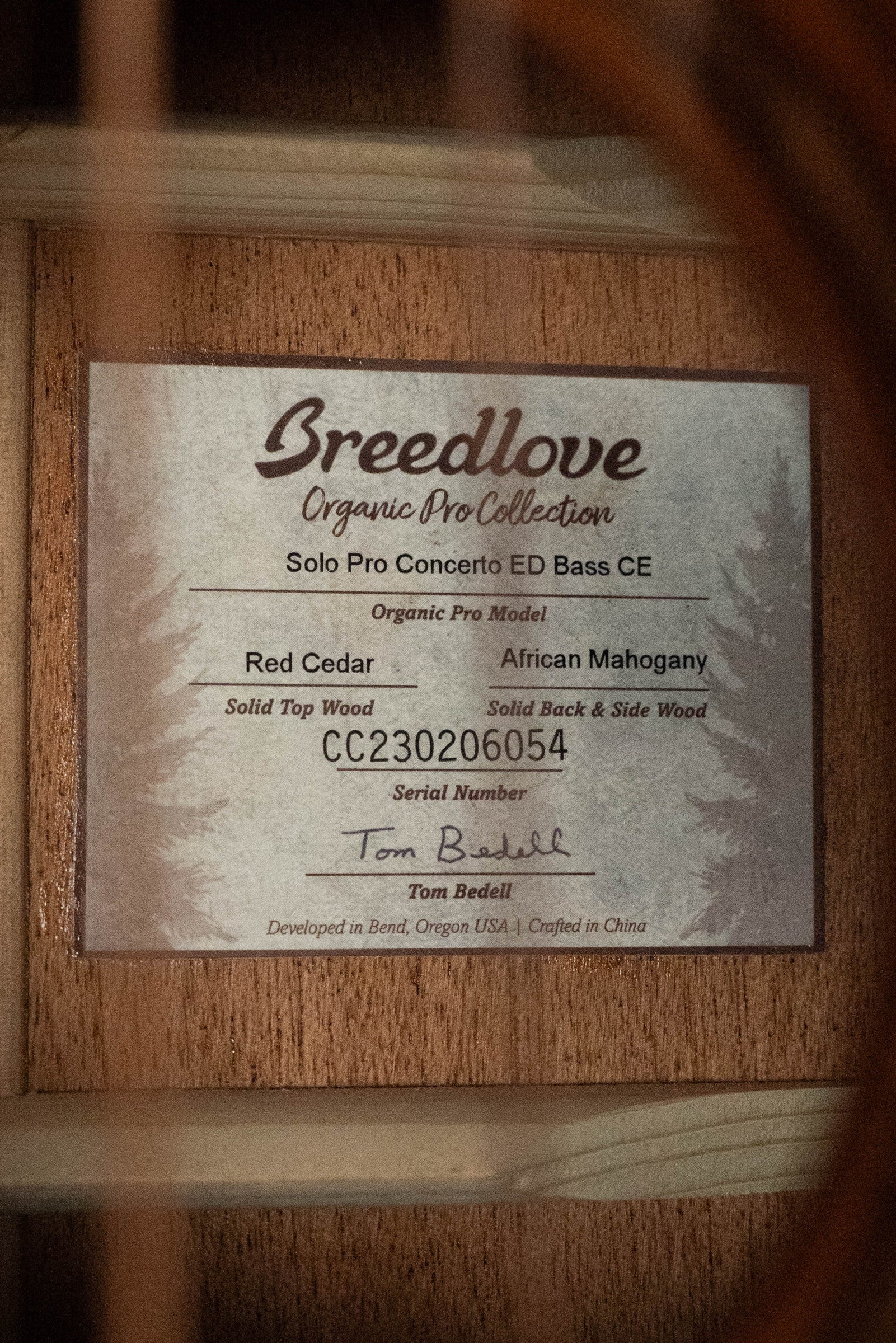 A close-up of a Breedlove Organic Solo Pro Concerto Red Cedar/African Mahogany Edgeburst Cutaway Acoustic Bass label, revealing model details, Fishman pickup, serial #6054, and Tom Bedell’s signature.