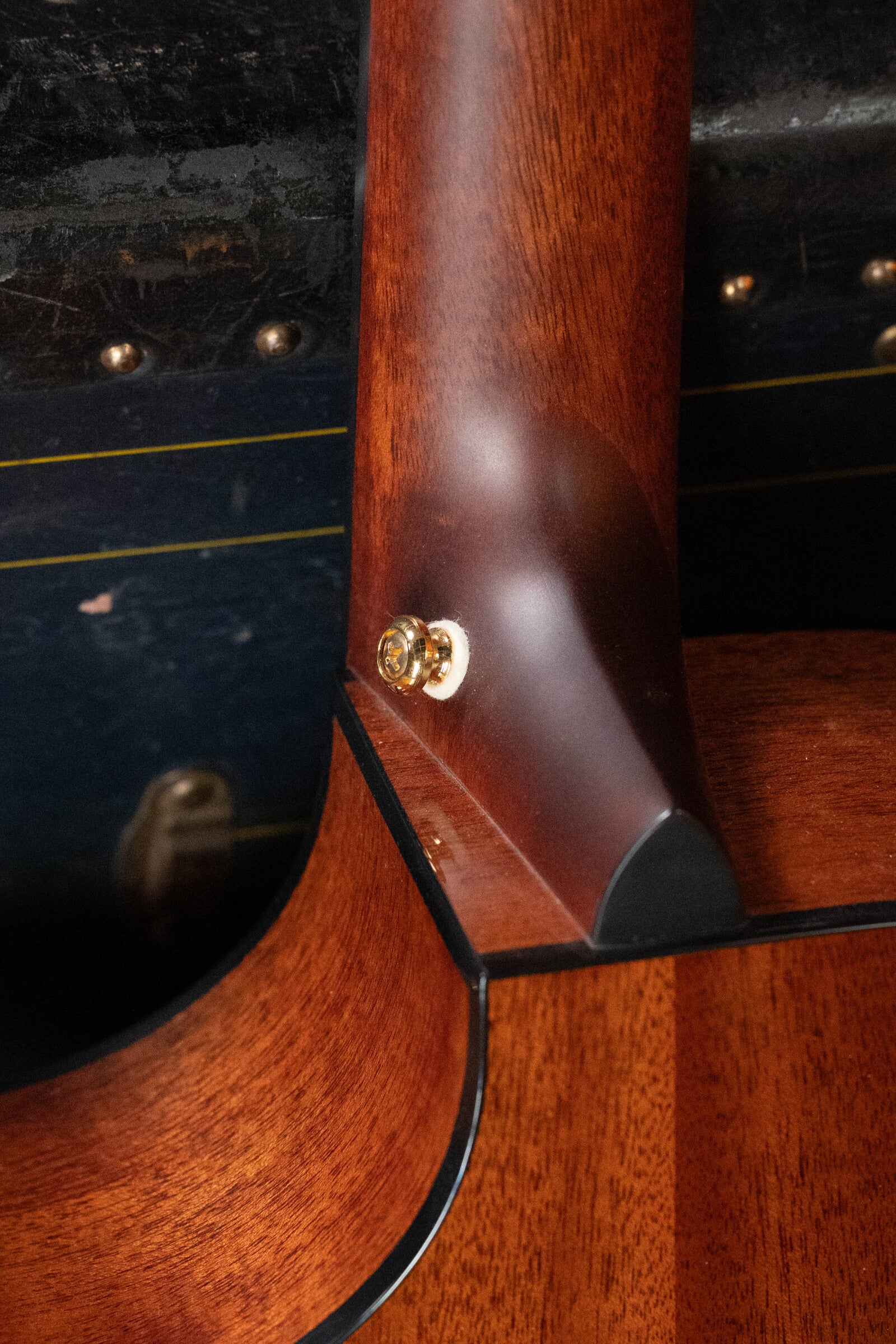 Close-up of the neck joint on a Breedlove Organic Solo Pro Concerto Red Cedar/African Mahogany Edgeburst Cutaway Acoustic Bass w/ Fishman Pickup, showing wood grain, gold strap button, and black binding against a dark textured background.