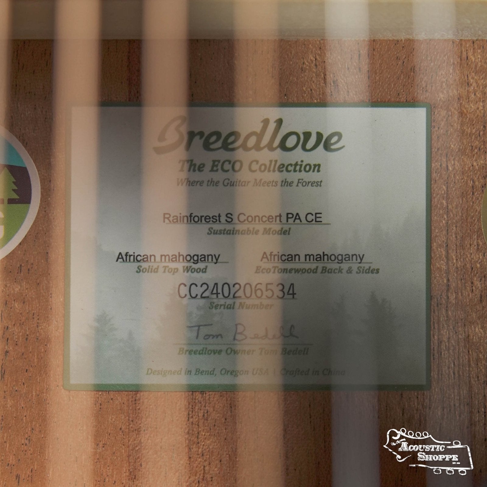 Close-up of a Breedlove Rainforest S Concert Papillon All Mahogany Cutaway Acoustic Guitars interior label, seen through the sound hole, with serial number and logos partly obscured by guitar strings.
