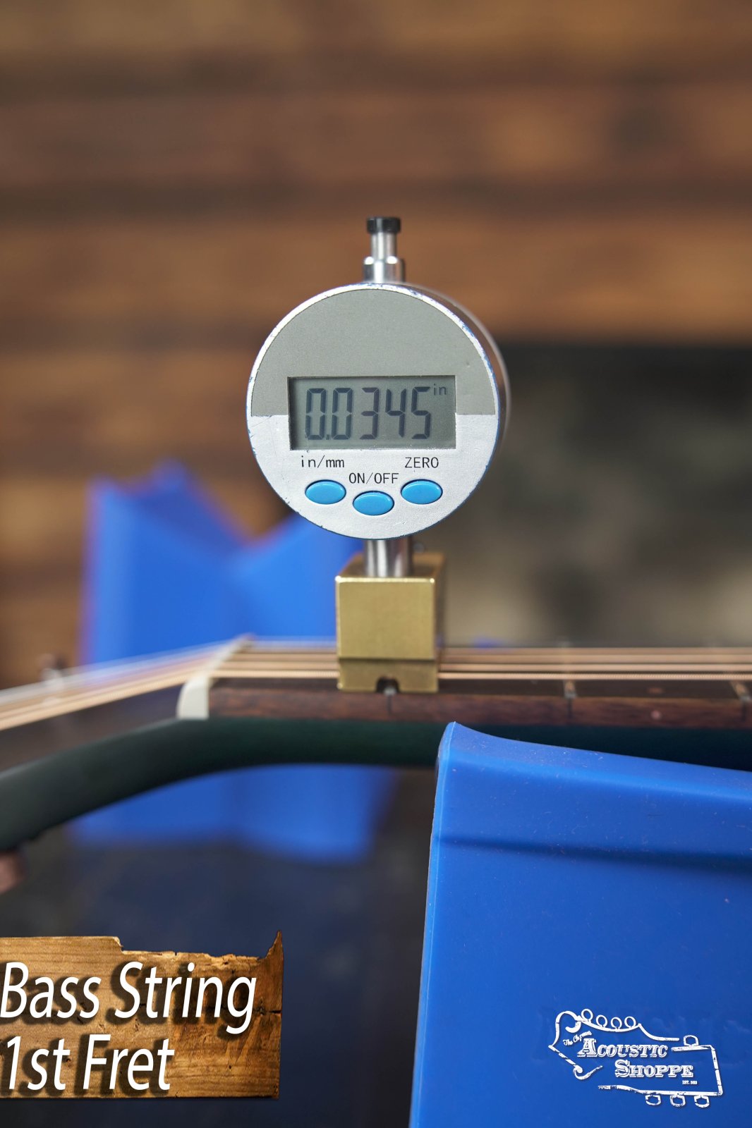 A digital caliper measures string height at the 1st fret of a Breedlove Rainforest S Concert Papillon All Mahogany Cutaway Acoustic Guitar w/Fishman Pickup #6534; EcoTonewood blue supports cradle the neck. Text: Bass String 1st Fret and Acoustic Shoppe.