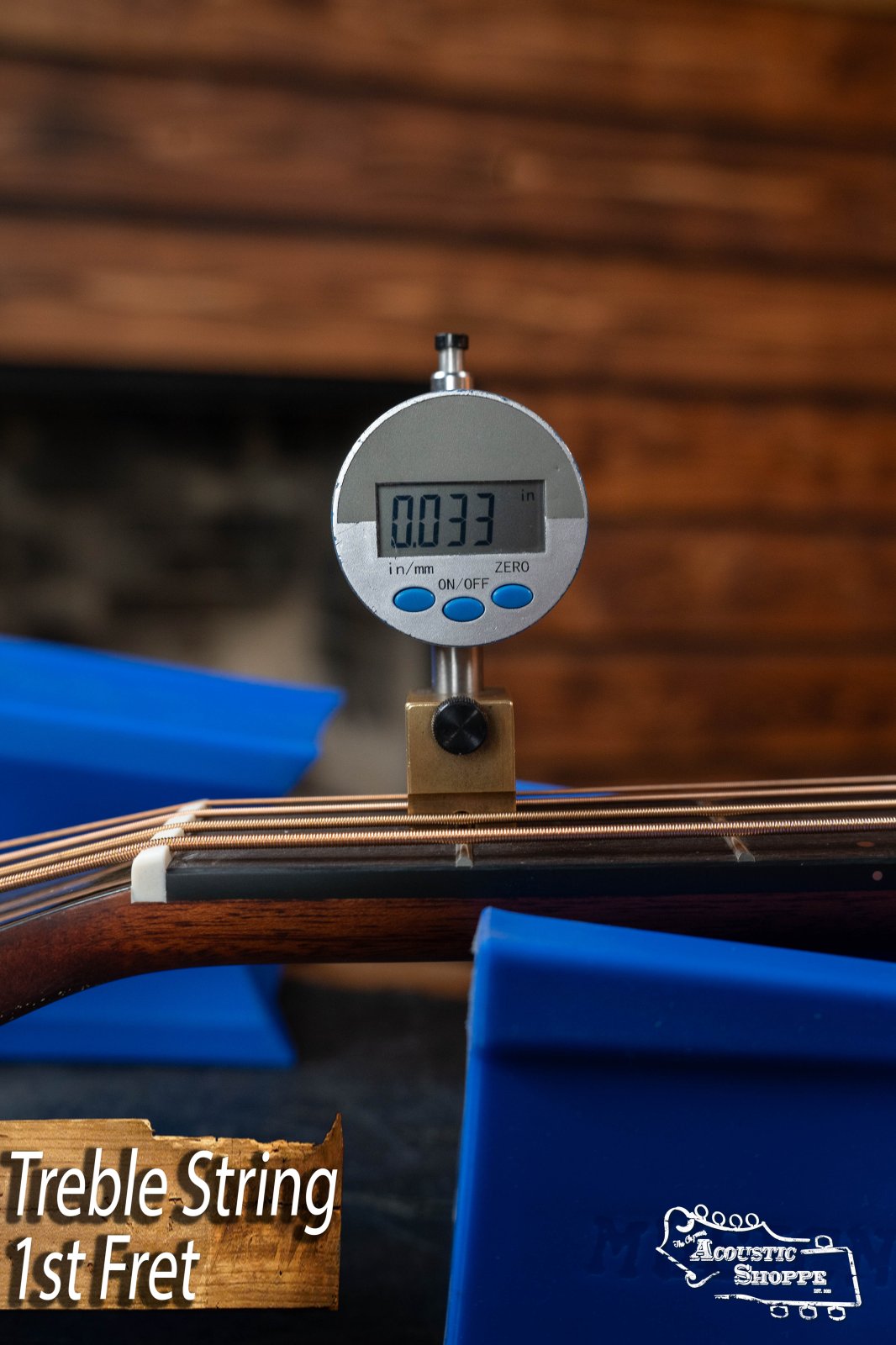 A digital gauge measuring 0.033" is placed on the 1st fret treble string of a Breedlove Organic Solo Pro Concerto Acoustic Bass, supported by blue stands, with “Treble String 1st Fret” text at the bottom left.