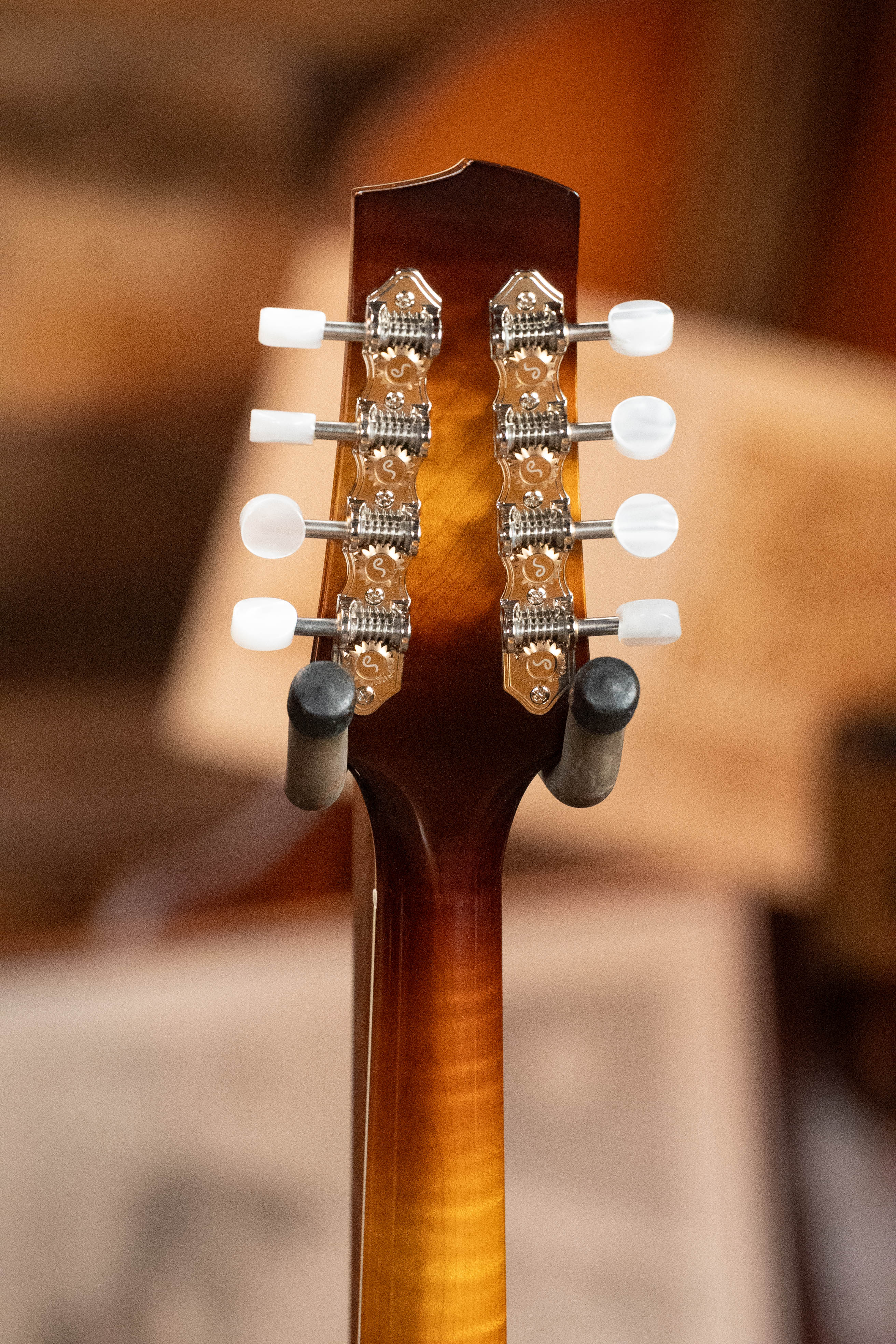 Close-up of the back of a Bulas Carpathian Spruce/Curly Maple Cremona Sunburst A-Style Mandolin #8129 headstock, showing six chrome tuning pegs with white knobs and intricate gears on a wooden neck.