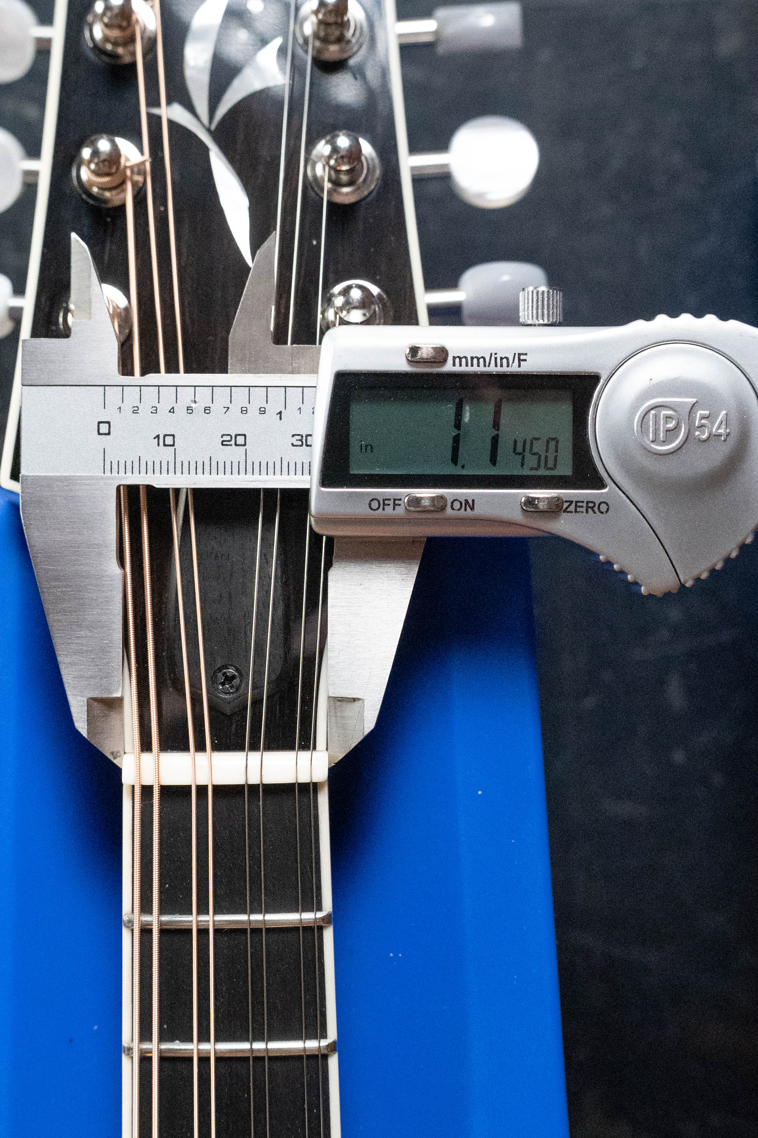 A digital caliper shows 1.450 inches while measuring the nut width of the Bulas Carpathian Spruce/Curly Maple Cremona Sunburst A-Style Mandolin #8129, which is supported by a blue holder.
