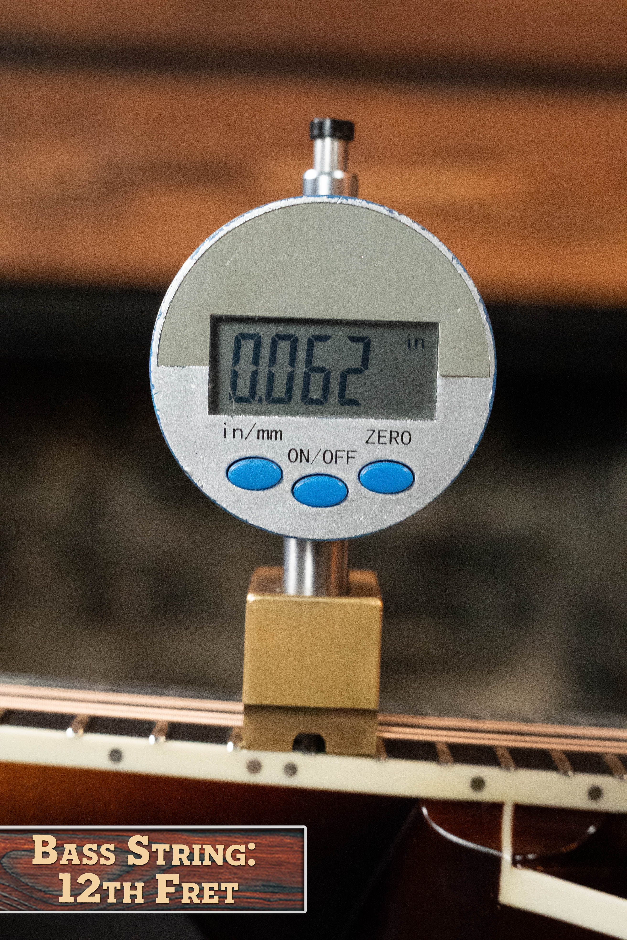 A digital gauge shows 0.062 inches at the 12th fret of a bass string. The Bulas Carpathian Spruce/Curly Maple Cremona Sunburst A-Style Mandolin #8129 is in the background, highlighting its beautiful finish.