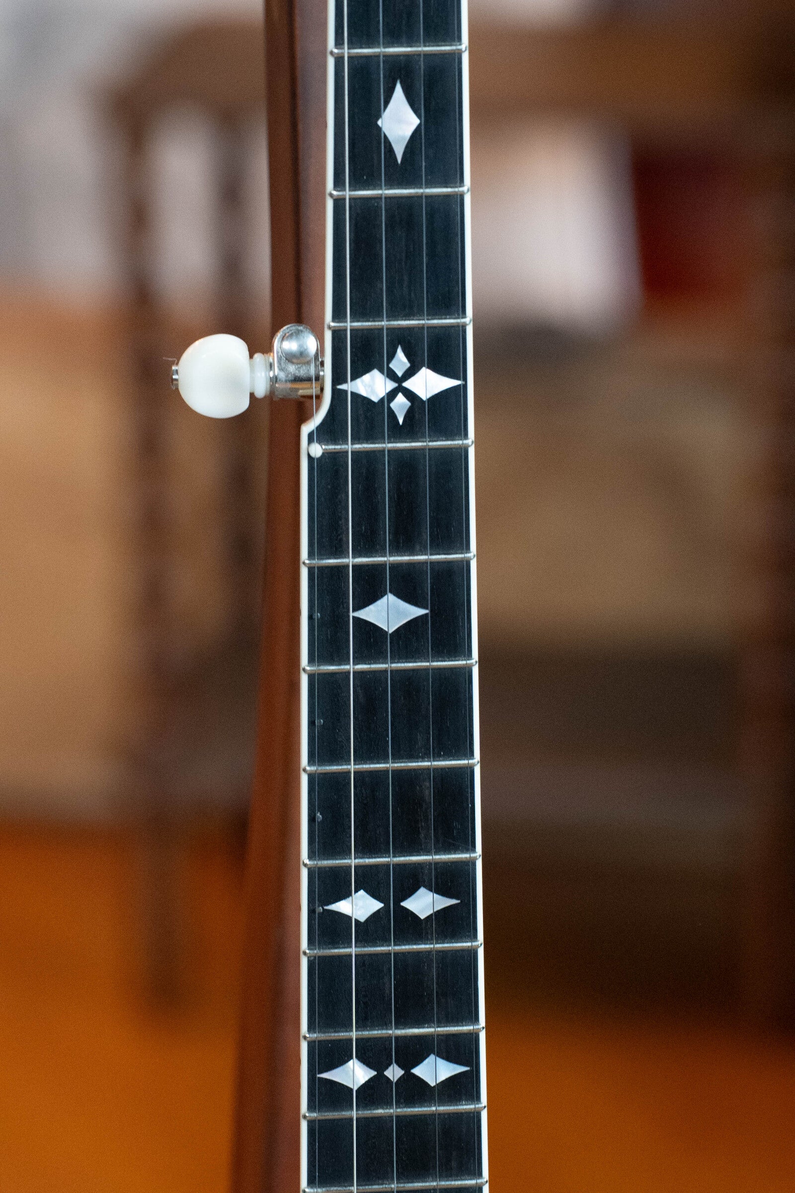 Close-up of the Bulas Standard 5-String Tobacco Sunburst Resonator Banjo #0676 shows its dark neck with white geometric inlays on the fretboard, a white side tuning peg, and a blurred background. Brand: Bulas.