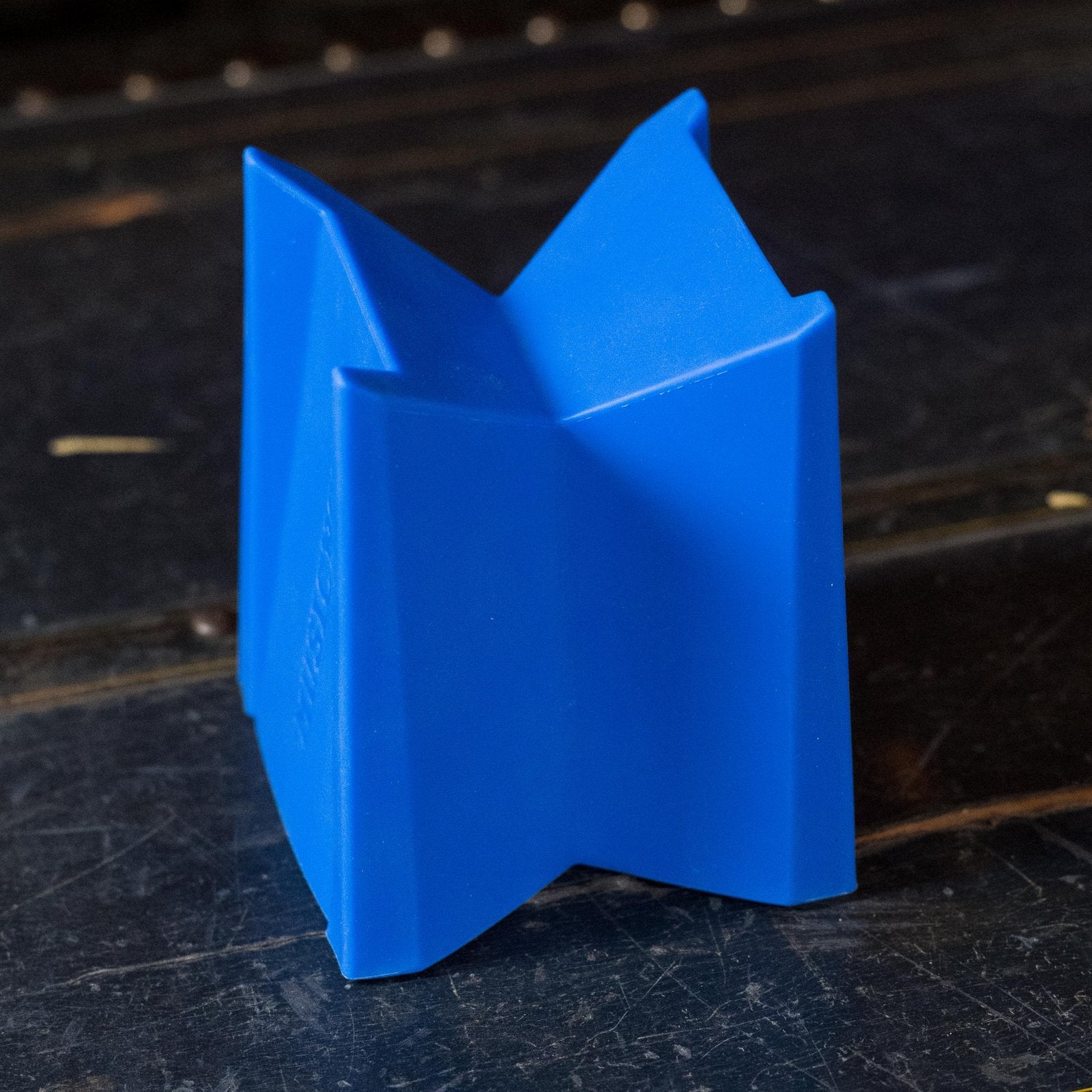 A blue, angular Music Nomad Cradle Cube (MN206) string instrument neck support stands upright on a dark, textured surface.