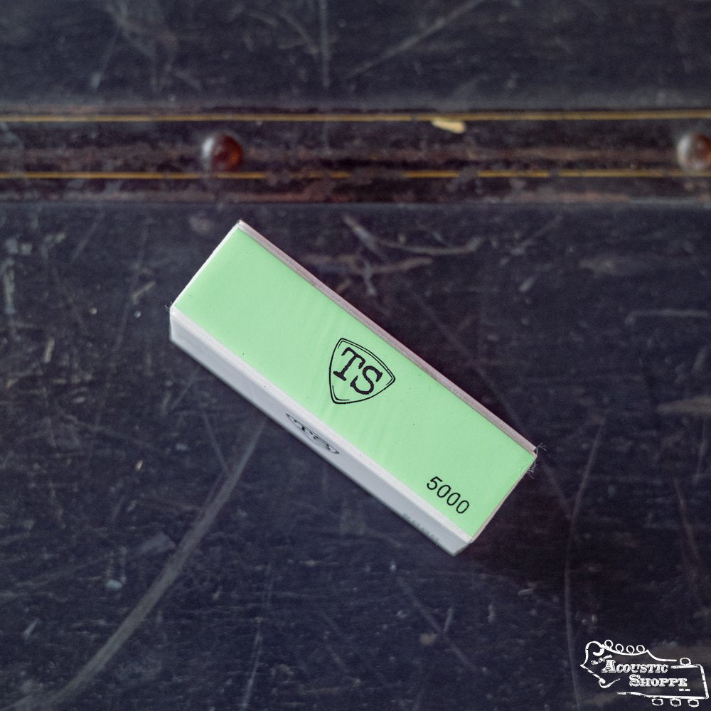 A green and white ToneSlabs Pick Buffer box labeled TS and 5000 rests on a scratched, dark surface with a metal strip. The Midwest Shoppe logo, a trusted acoustic shop brand, is visible in the bottom right corner.