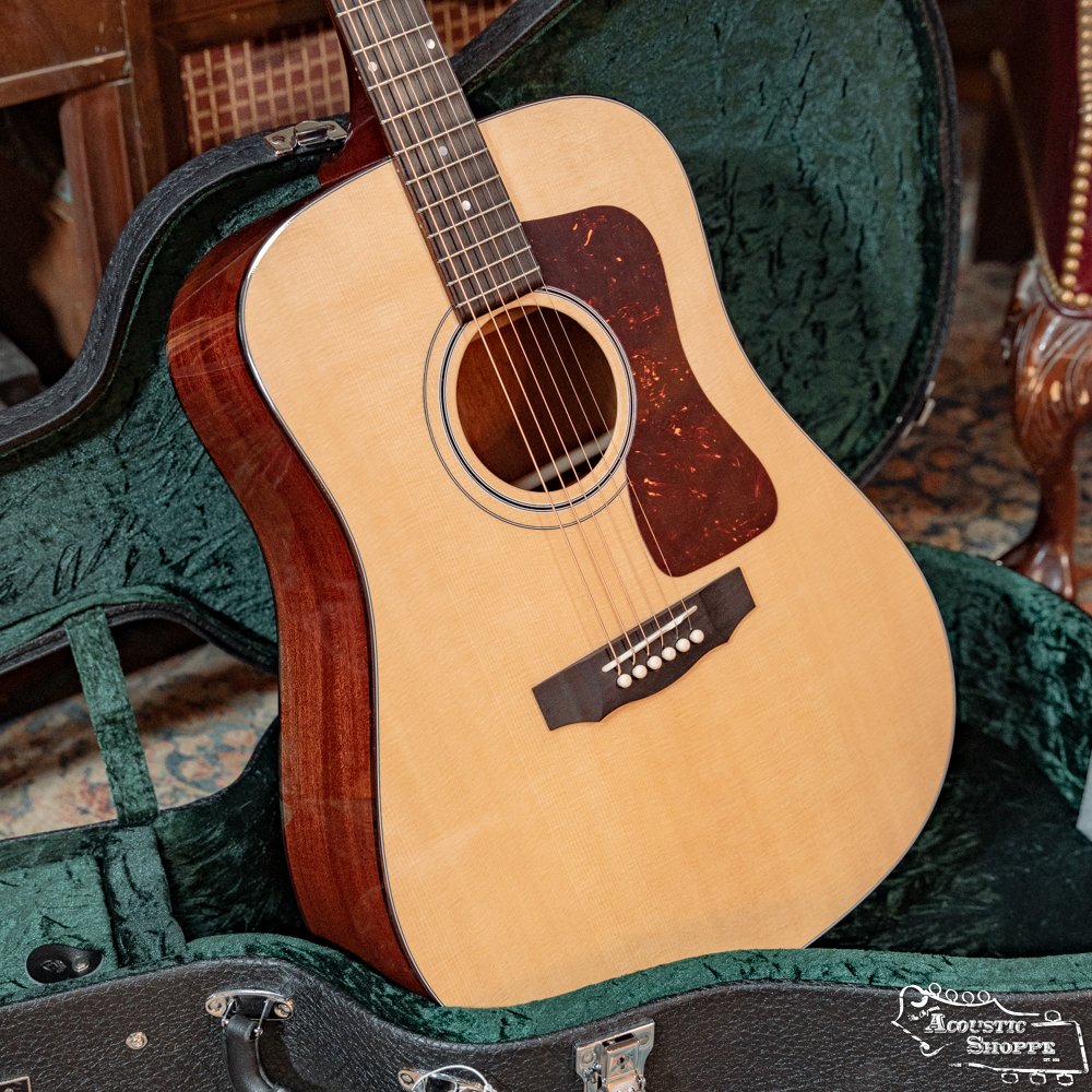 A Guild Guitars USA D-40 Traditional Sitka Spruce/African Mahogany Natural Top Dreadnought #1106 with a light top, dark sides, and tortoiseshell pickguard stands upright in an open, green-lined hard case.