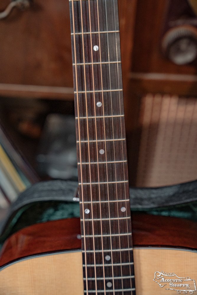 Close-up of a Guild Guitars USA D-40 Traditional Sitka Spruce/African Mahogany Natural Top Dreadnought #1106 neck and fretboard with dot inlays, showing the upper body and soundhole. Blurred background includes furniture and books.