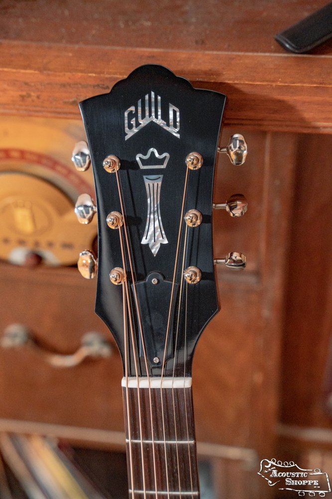 Close-up of the Guild Guitars USA D-40 Traditional Sitka Spruce/African Mahogany Natural Top Dreadnought #1106 headstock, showing six tuning pegs and crowned Guild logo, set against a wooden cabinet with decorative details.