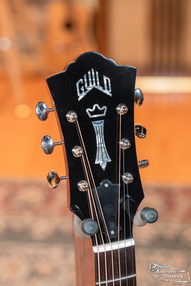 Close-up of the Guild Guitars USA D-40 Traditional Sitka Spruce/African Mahogany Natural Top dreadnought (#1106) headstock, showing chrome tuners, white logo, and crown inlay against a softly blurred warm-toned background.
