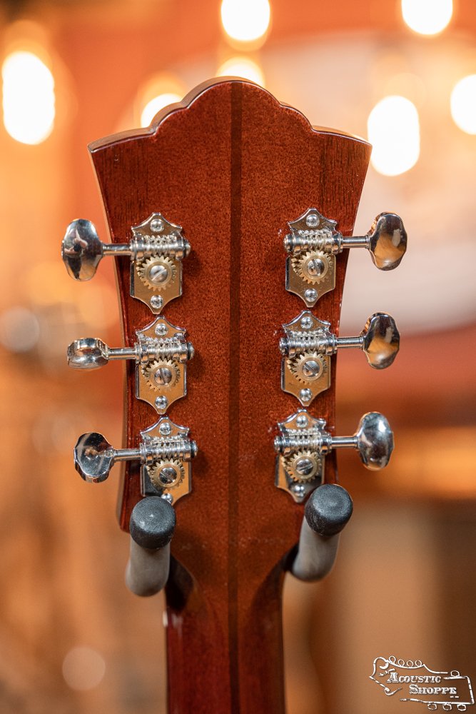 Close-up of the Guild Guitars USA D-40 Traditional Sitka Spruce/African Mahogany Natural Top Dreadnought #1106 headstock, featuring six silver tuning pegs and ornate hardware, set against a backdrop of warm, blurred lights.