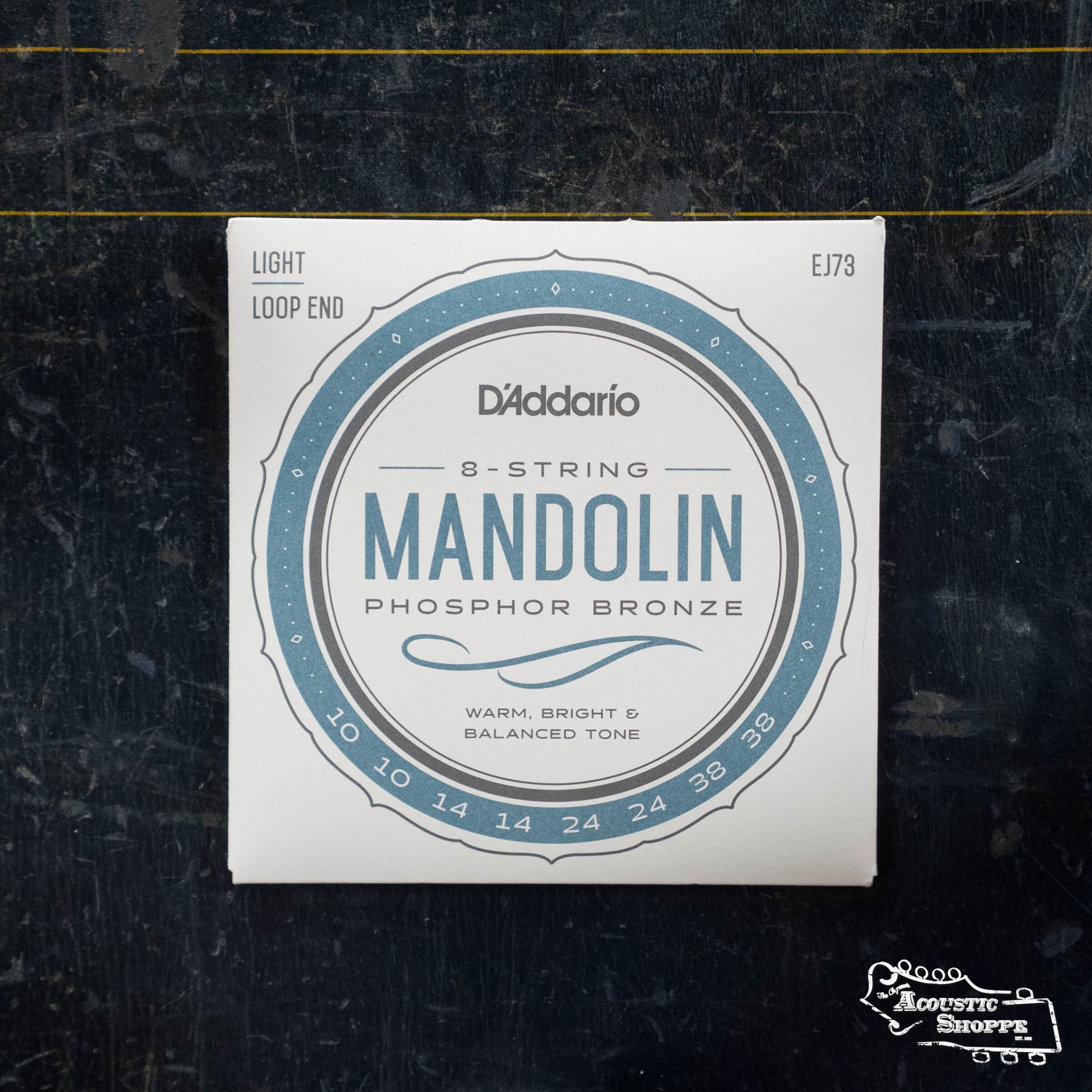 A pack of D'Addario EJ73 Mandolin Strings, Phosphor Bronze, Light (10-38), for 8-string mandolins is displayed on a dark surface. The packaging features “LIGHT,” “LOOP END,” and “Warm, Bright & Balanced Tone.”.