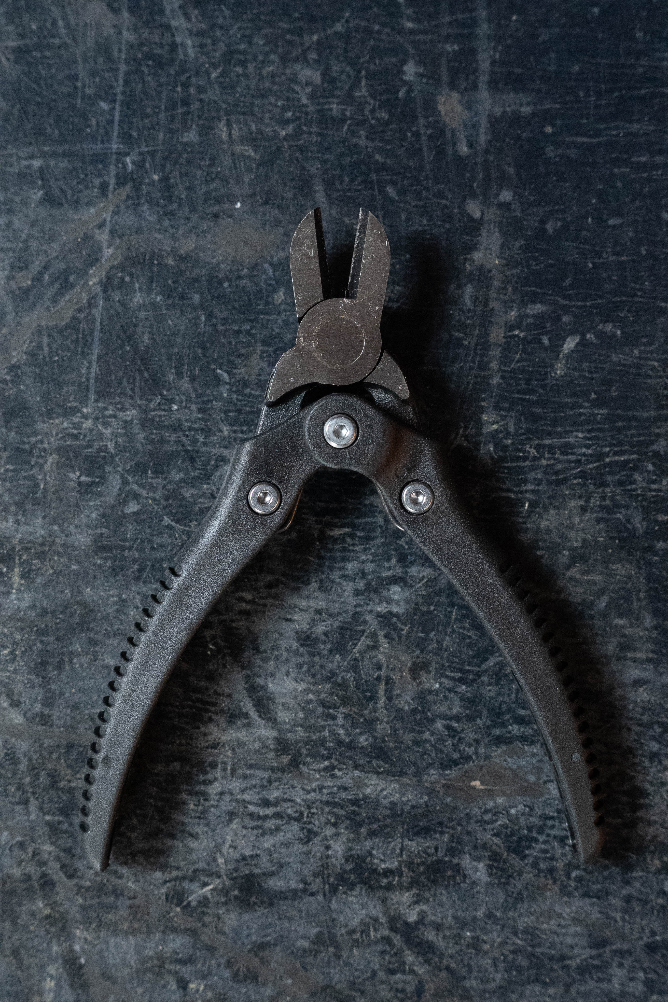 A pair of D'Addario wire cutters from the D'Addario Tour Grade String Changing Kit, ideal for cutting strings, rests on a scratched dark surface with textured handles and closed jaws spread in a V-shape.