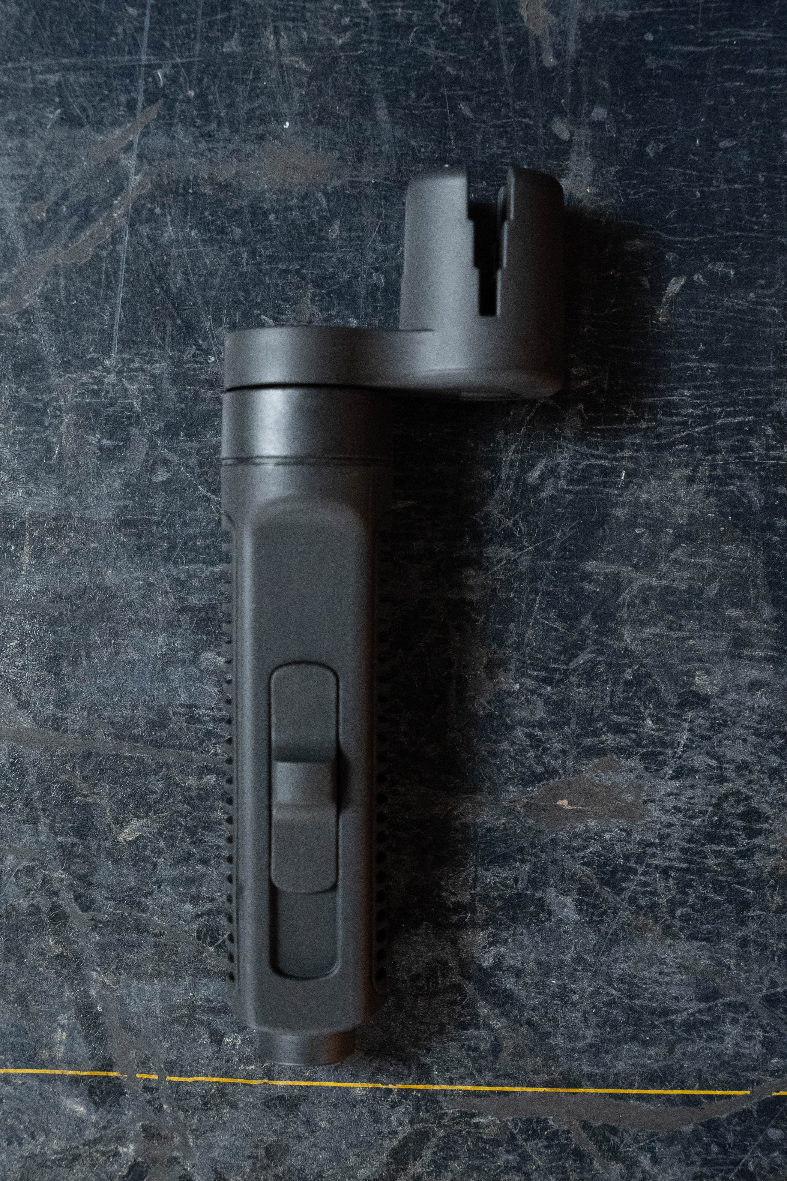 A D'Addario Tour Grade String Changing Kit toolโa black plastic string cutter and bridge pin pullerโrests on a worn, dark textured surface.