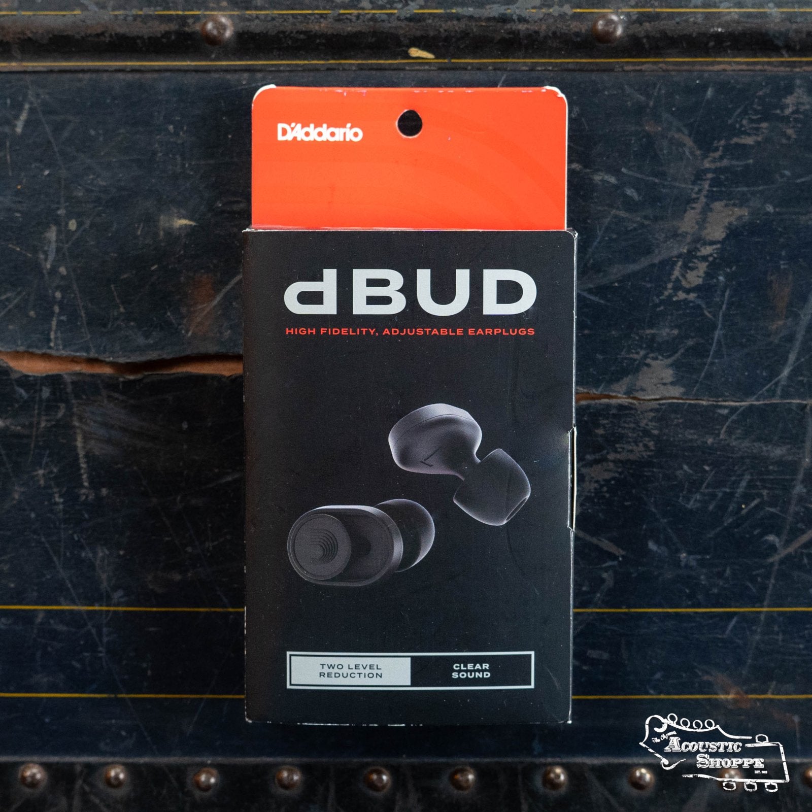 A box of DAddario PW-DBUDHP-01 Bud Premium Hearing Protection earplugs rests on a dark, textured surface. The packaging by DAddario features two-level sound reduction and clear audio for ideal musician hearing protection.
