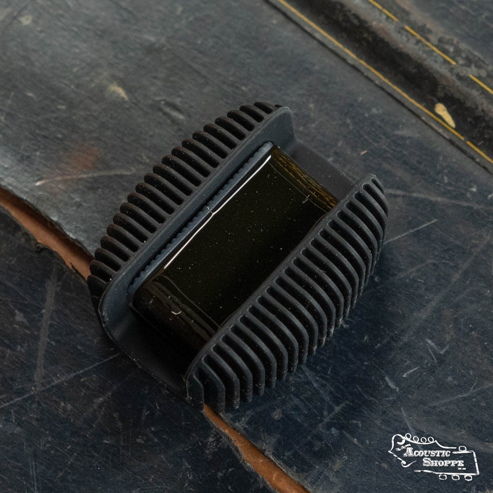 A D'Addario Rosin Guard with Natural Dark Rosin DRGBK-VR300, a black rectangular accessory, rests on a worn dark wooden surface. The Acoustic Shoppe logo appears in the bottom right corner.