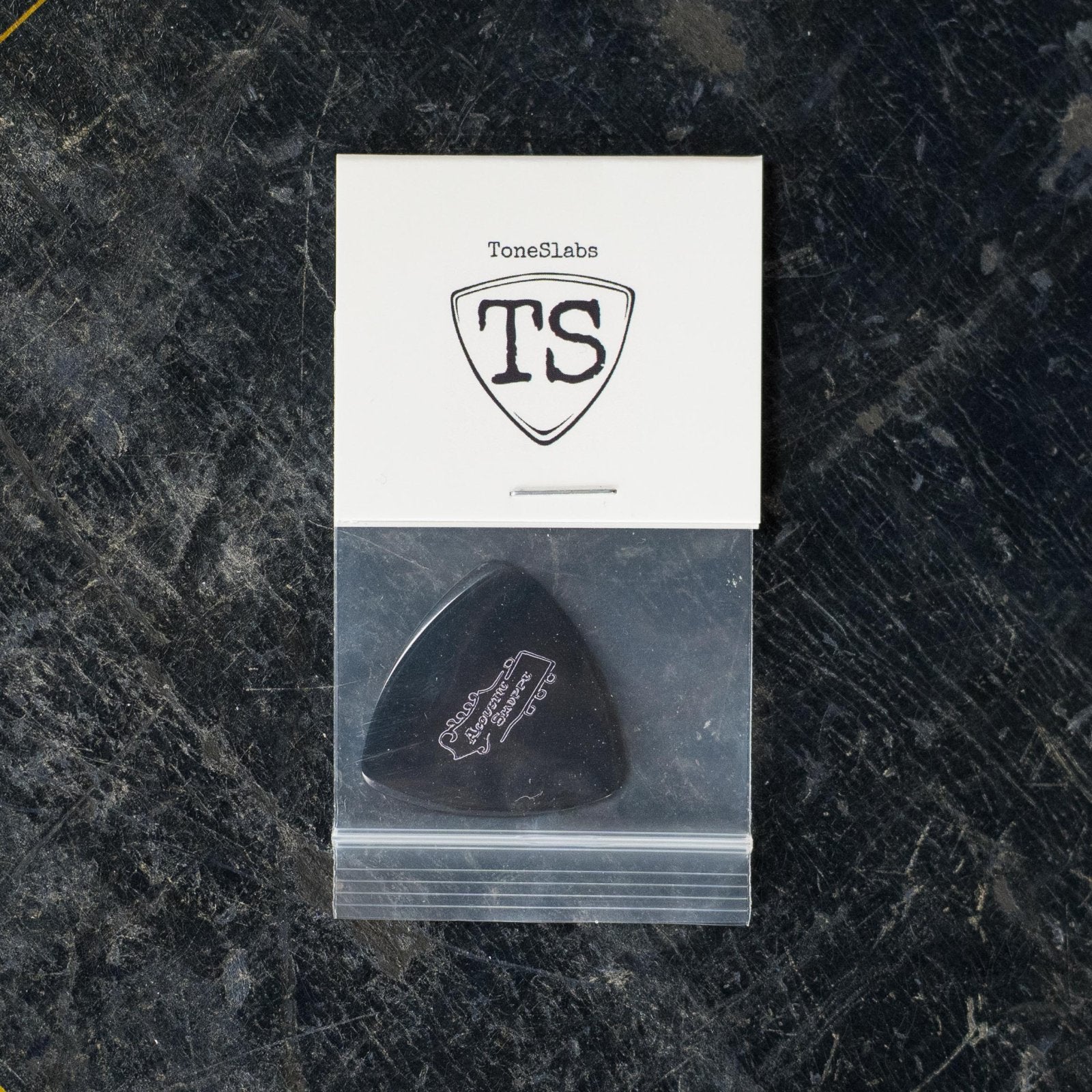 The ToneSlabs Darth Tone Series Tweener 1.3mm pick comes in a clear bag, stapled to a branded white card, and displayed on a dark surface—perfect for instrument dealers seeking personalized recommendations.
