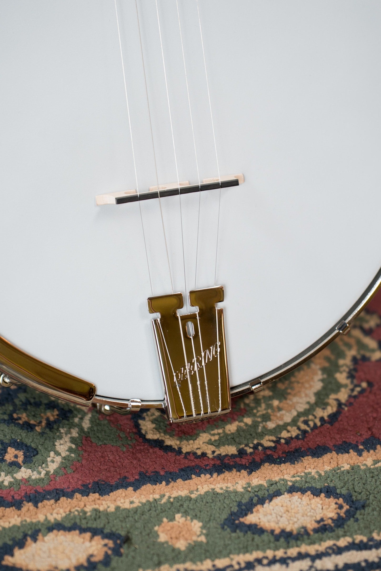 Close-up of the strings and tailpiece of a Deering Banjos Artisan Goodtime 5-String Openback Banjo #6251 resting on a patterned, multicolored rug.