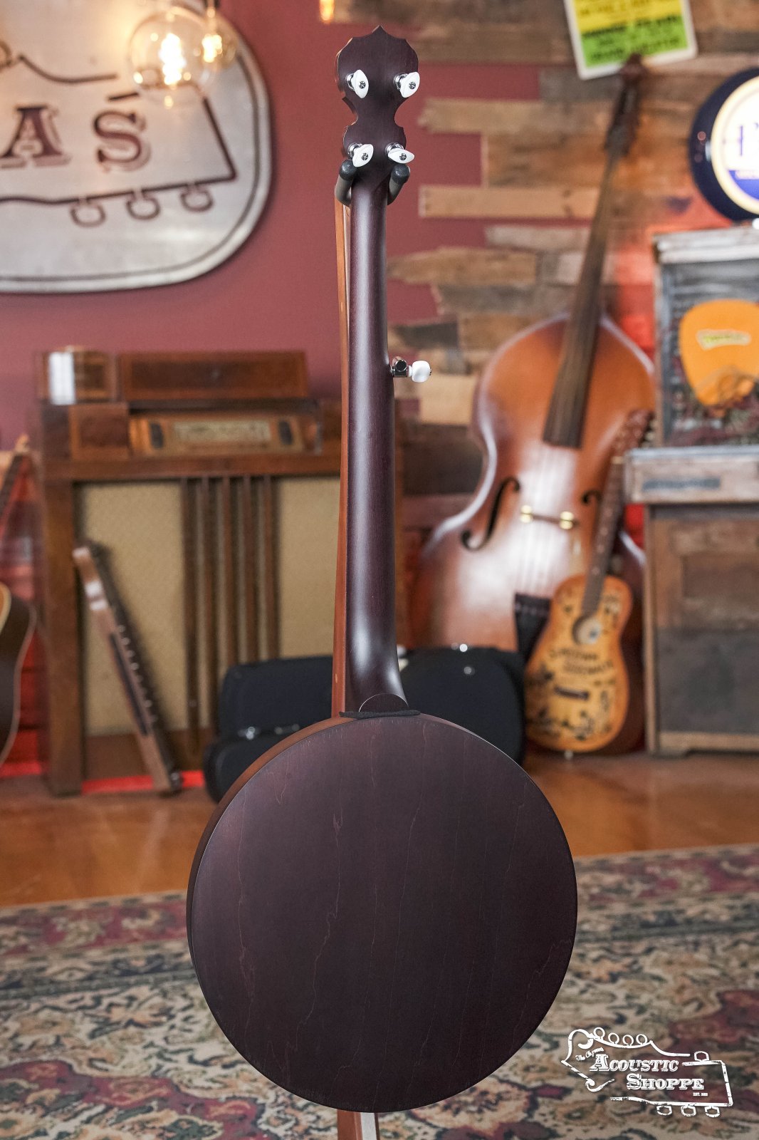 The Deering Banjos Artisan Goodtime Two 5-String Banjo with Resonator #8977 is displayed upright with its resonator back facing the camera in a cozy music shop, surrounded by other stringed instruments and vintage decor.
