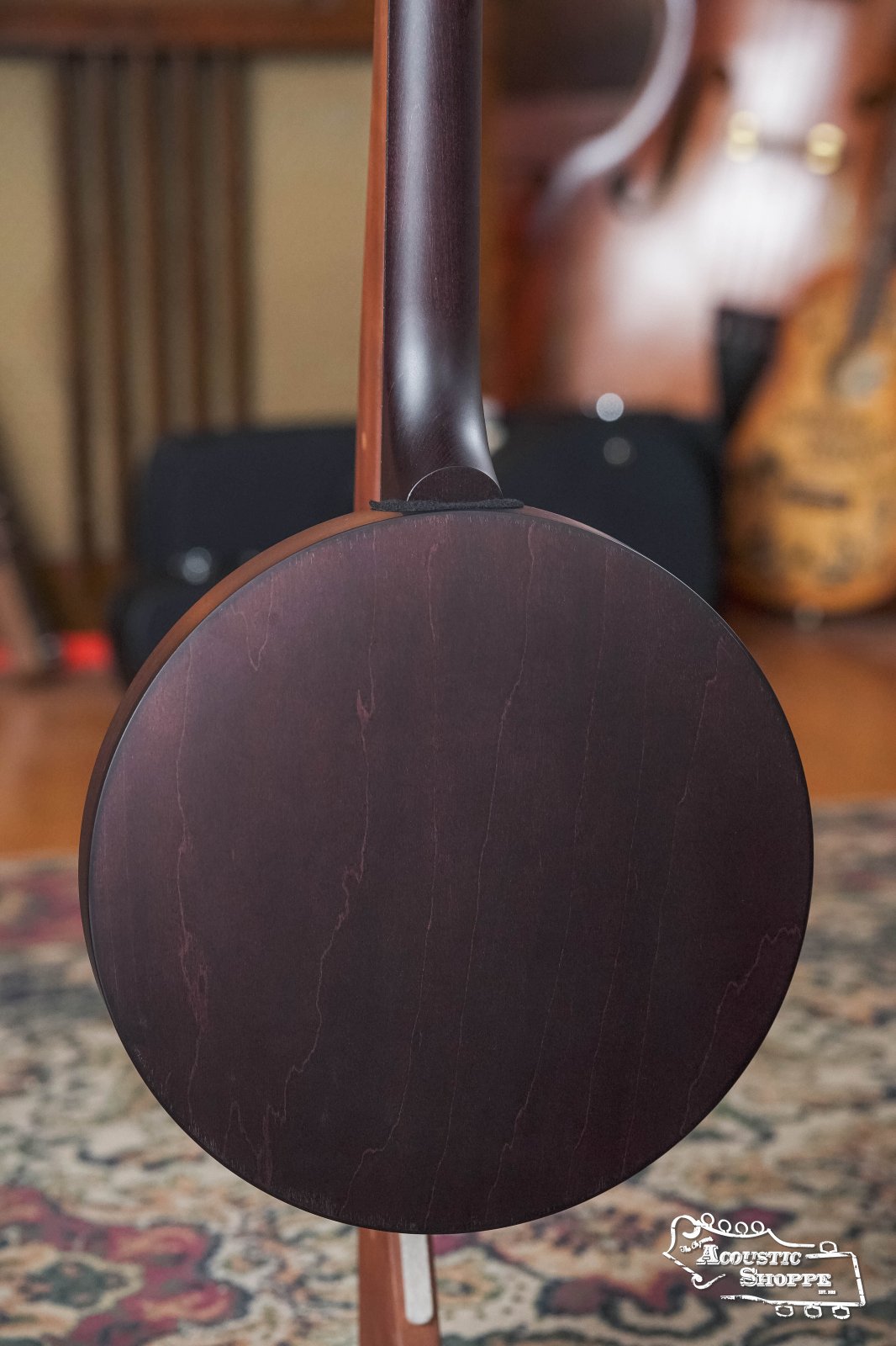 A close-up of the Deering Artisan Goodtime Two 5-String Banjo with Resonator #8977 by Deering Banjos shows its smooth, dark wooden resonator back. The blurred background features musical instruments and a patterned rug. The Acoustic Shoppe logo appears in the corner.
