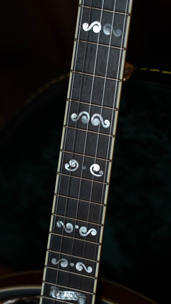 Close-up of a Deering Banjos Calico 5 String Curly Maple Resonator Banjo w/Spikes Installed (#AX45) shows its dark wood fretboard with ornate mother-of-pearl inlays and a glimpse of the curly maple body in the background.