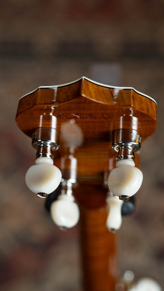Close-up of the tuning pegs on the Deering Banjos Calico 5 String Curly Maple Resonator Banjo w/Spikes Installed #AX45, showing its glossy wood finish and white metallic pegs against a blurred background.