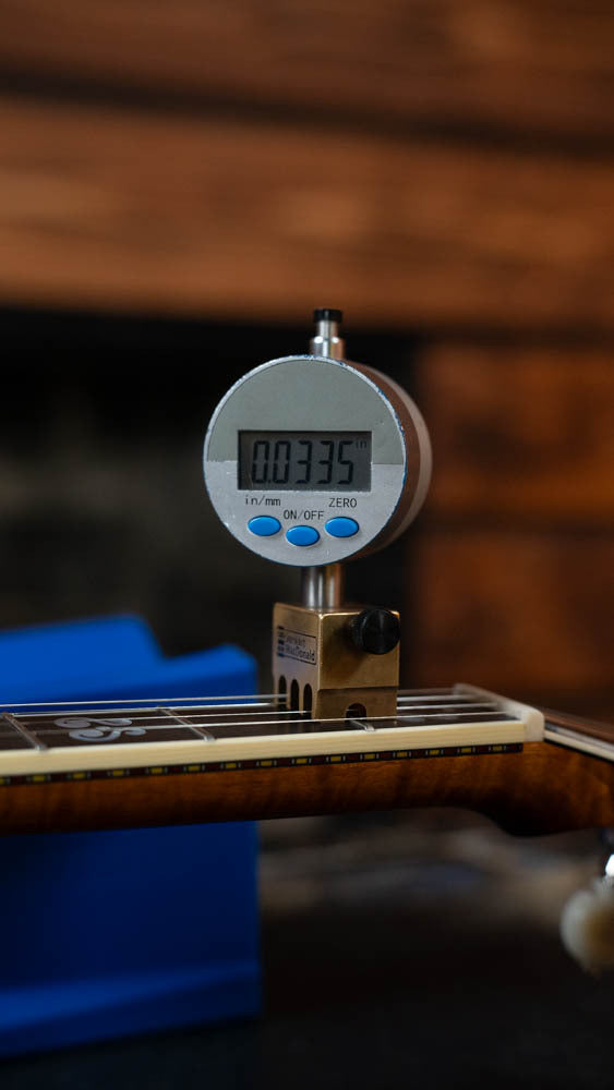 A digital indicator gauge shows a reading of 0.0335 inches when measuring the string height above the fretboard on a Deering Calico 5 String Curly Maple Resonator Banjo w/Spikes Installed #AX45 by Deering Banjos.