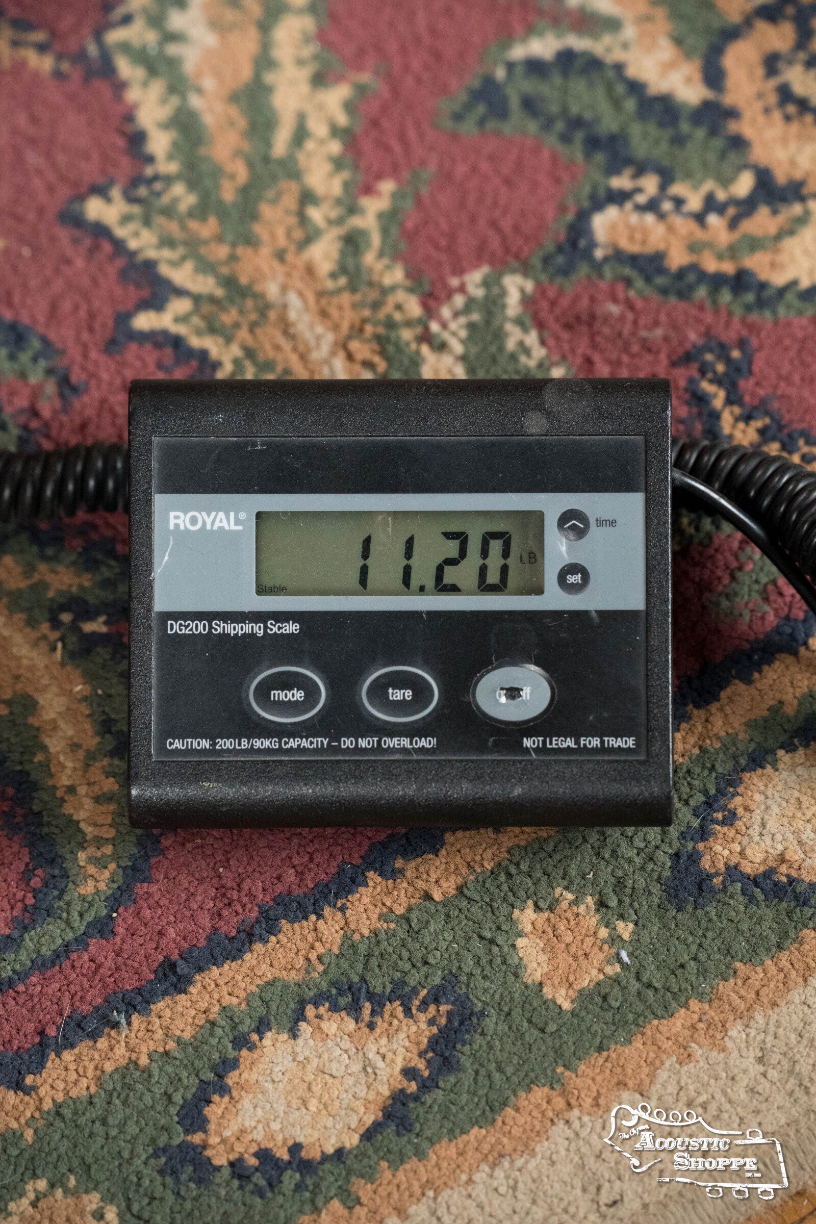 A digital shipping scale labeled ROYAL DG200 shows the Deering Banjos Golden Wreath 5 String Resonator Banjo #AU47 weighs 11.20 pounds on patterned carpet—ideal for weighing instruments like this banjo model.