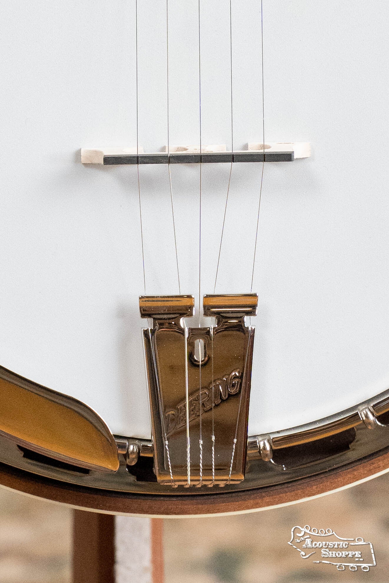 Close-up of the Deering Golden Wreath 5 String Resonator Banjo #AU47 tailpiece and strings, featuring the Deering Banjos brand engraved on metal. The white drumhead and part of the wooden rim are also in view.