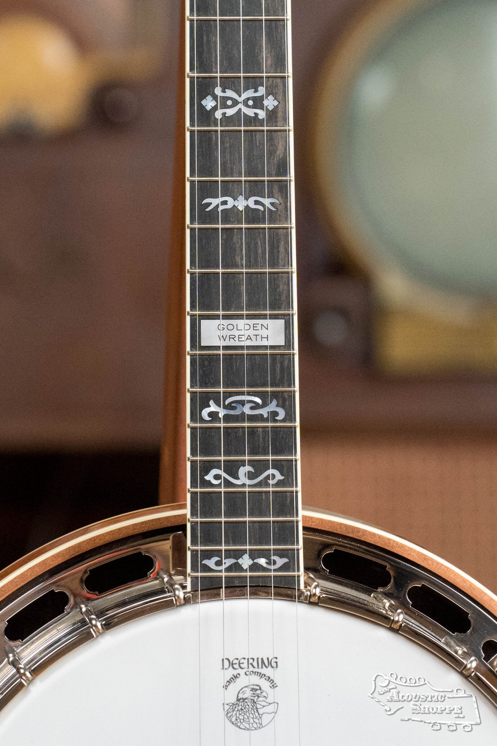 Close-up of a Deering Banjos Golden Wreath 5 String Resonator Banjo #AU47, highlighting ornate neck inlays and GOLDEN WREATH on the fret, with the Deering logo on the banjo head and a softly blurred background.
