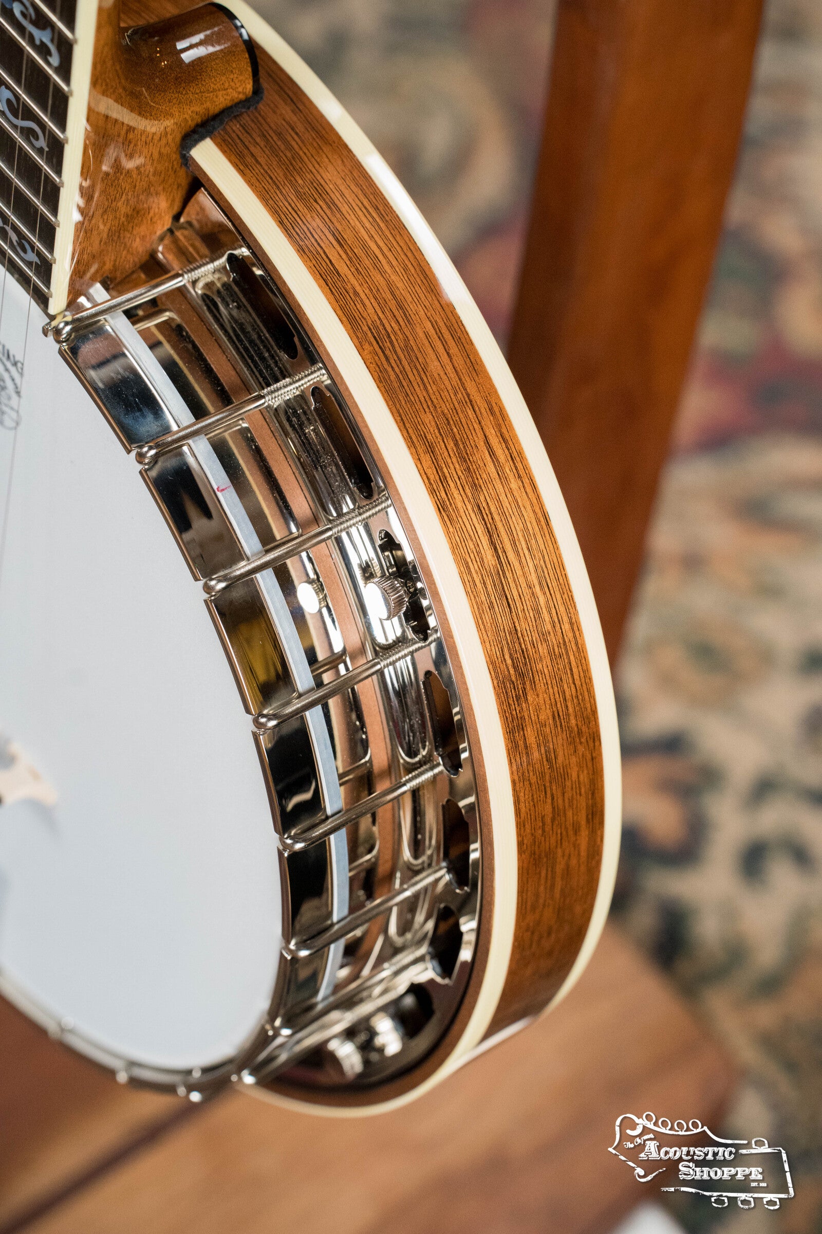 Close-up of a Deering Banjos Golden Wreath 5 String Resonator Banjo #AU47 showing its wooden body and shiny metal rim against a blurred background, with The Acoustic Shoppe logo in the bottom right corner.