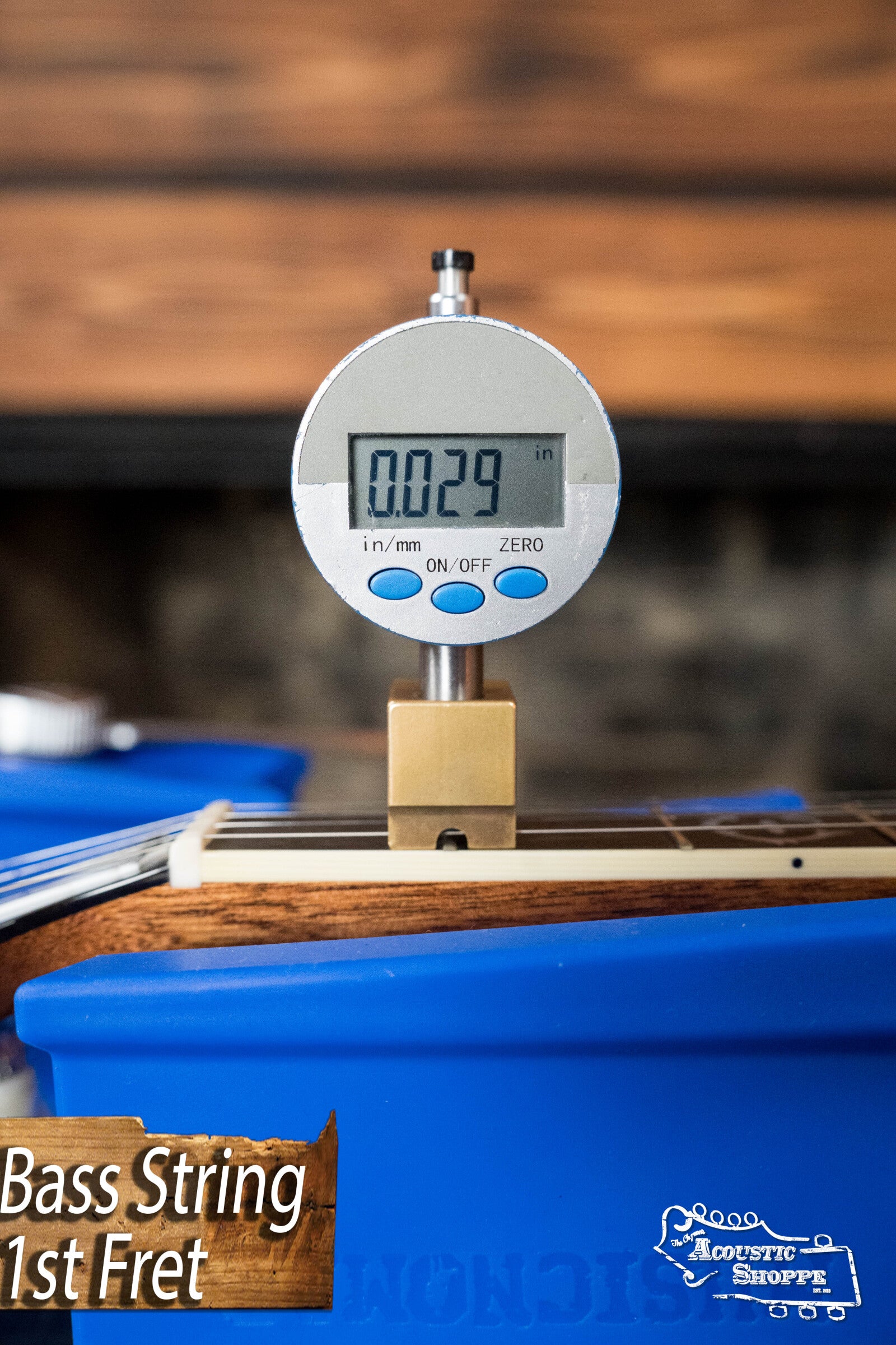 A digital gauge measures a bass strings height at the 1st fret (0.029 inches) on a Deering Golden Wreath 5 String Resonator Banjo #AU47, resting in a blue holder—ideal for Bluegrass banjo setups by Deering Banjos.