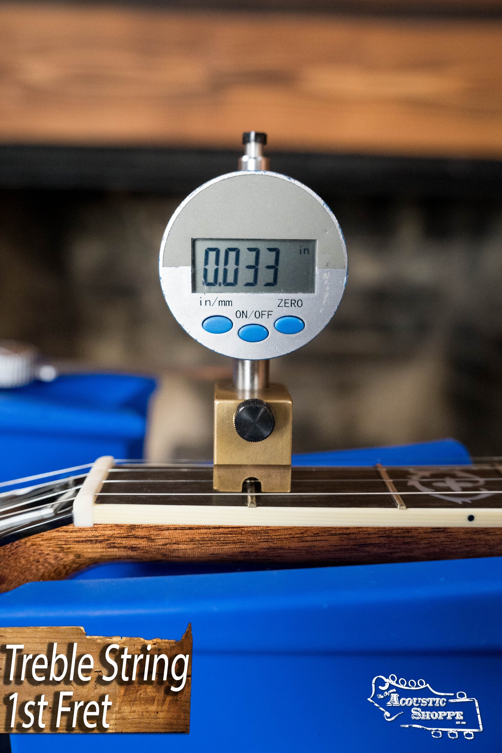 A digital gauge shows the treble string height at the 1st fret as 0.033 on a Deering Golden Wreath 5 String Resonator Banjo #AU47 by Deering Banjos. The banjo rests on a blue support with text: “Treble String 1st Fret.”.