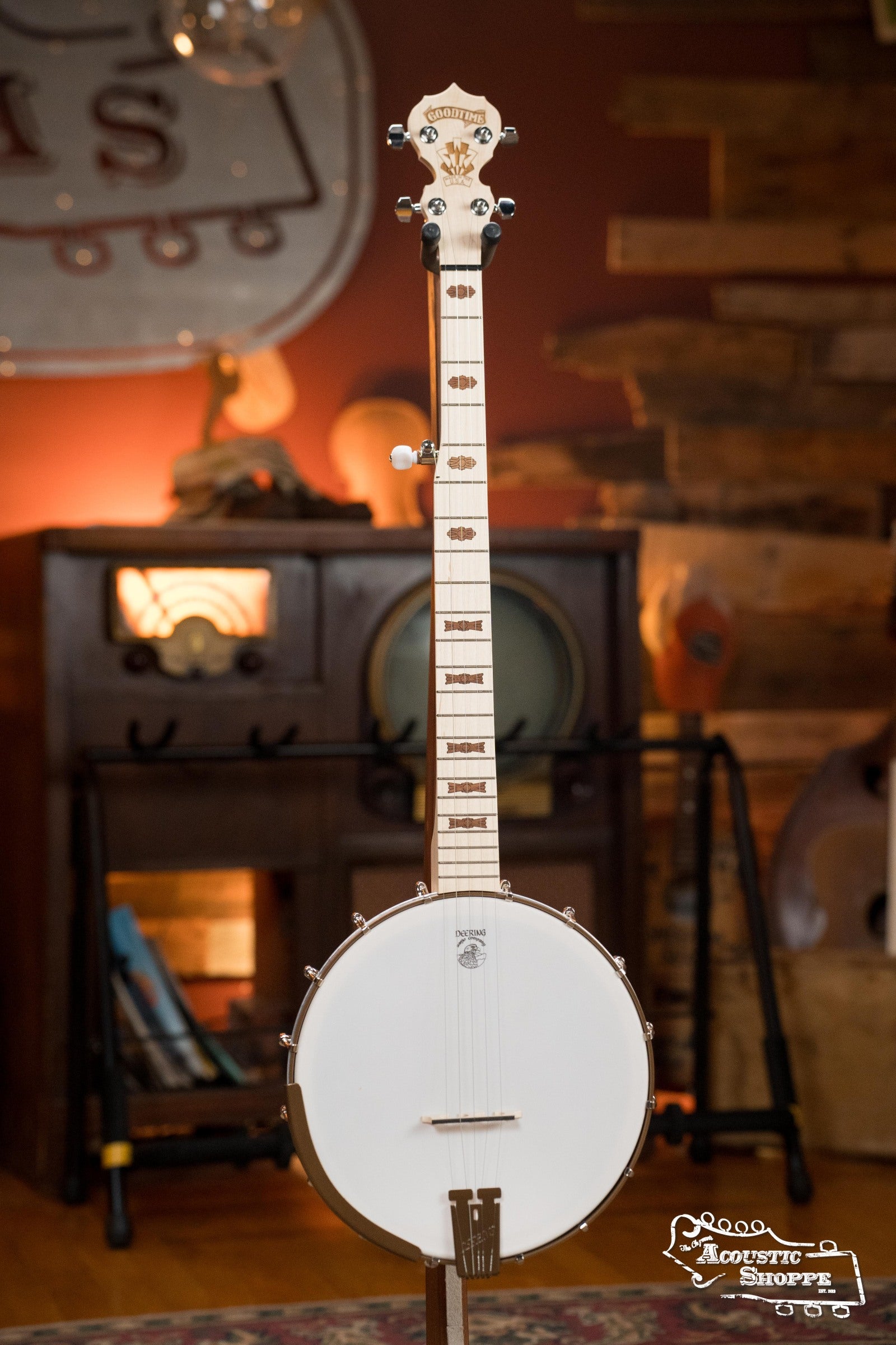 The Deering Goodtime Deco 5-String Banjo #52407 by Deering Banjos stands upright on a wooden floor in a warmly lit room, surrounded by vintage furniture and music equipment.