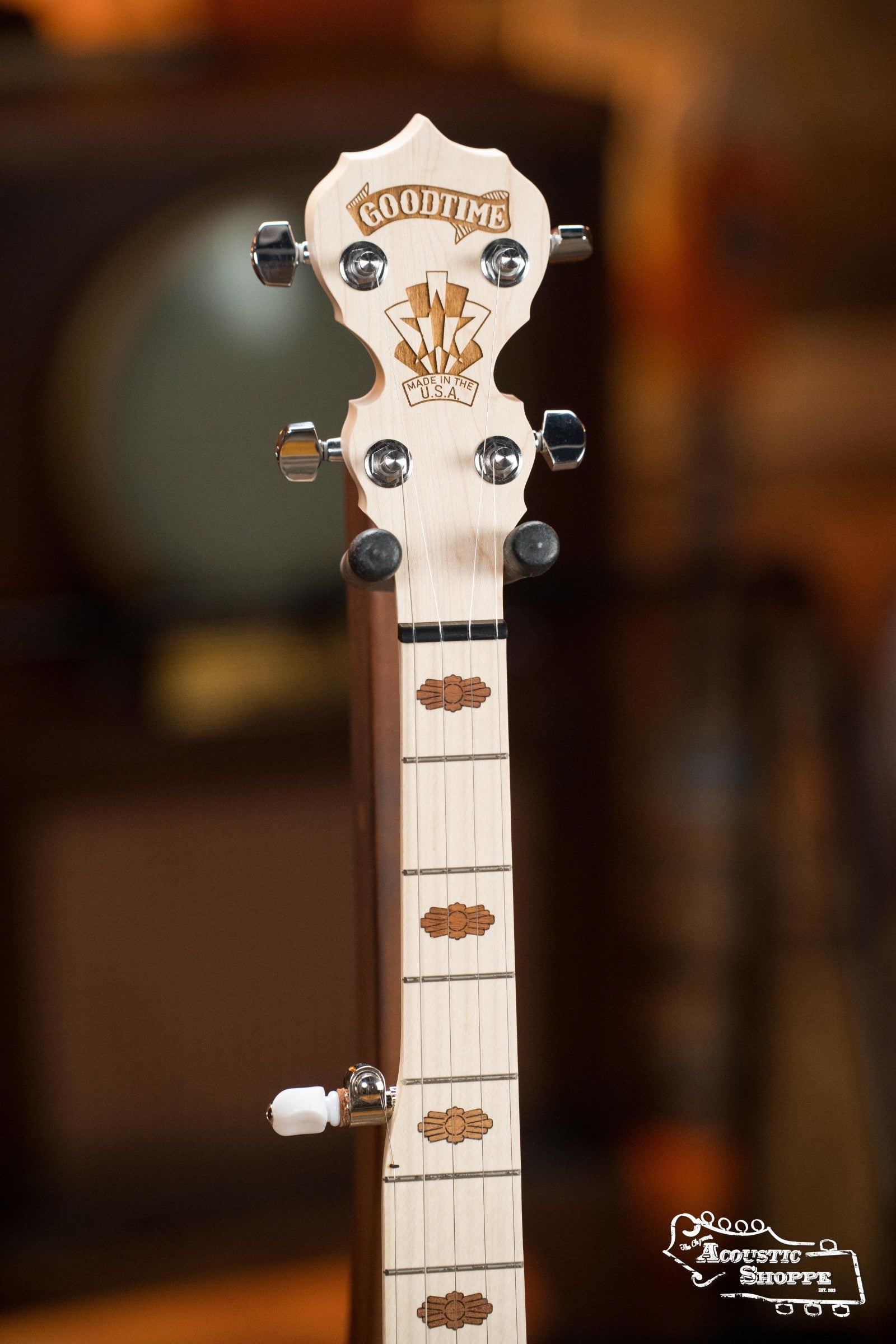 A close-up of the Deering Goodtime Deco 5-String Banjo #52407 headstock and upper fretboard from Deering Banjos, featuring light wood with engraved inlays. The background is blurred, with the Acoustic Shoppe logo in the lower right corner.