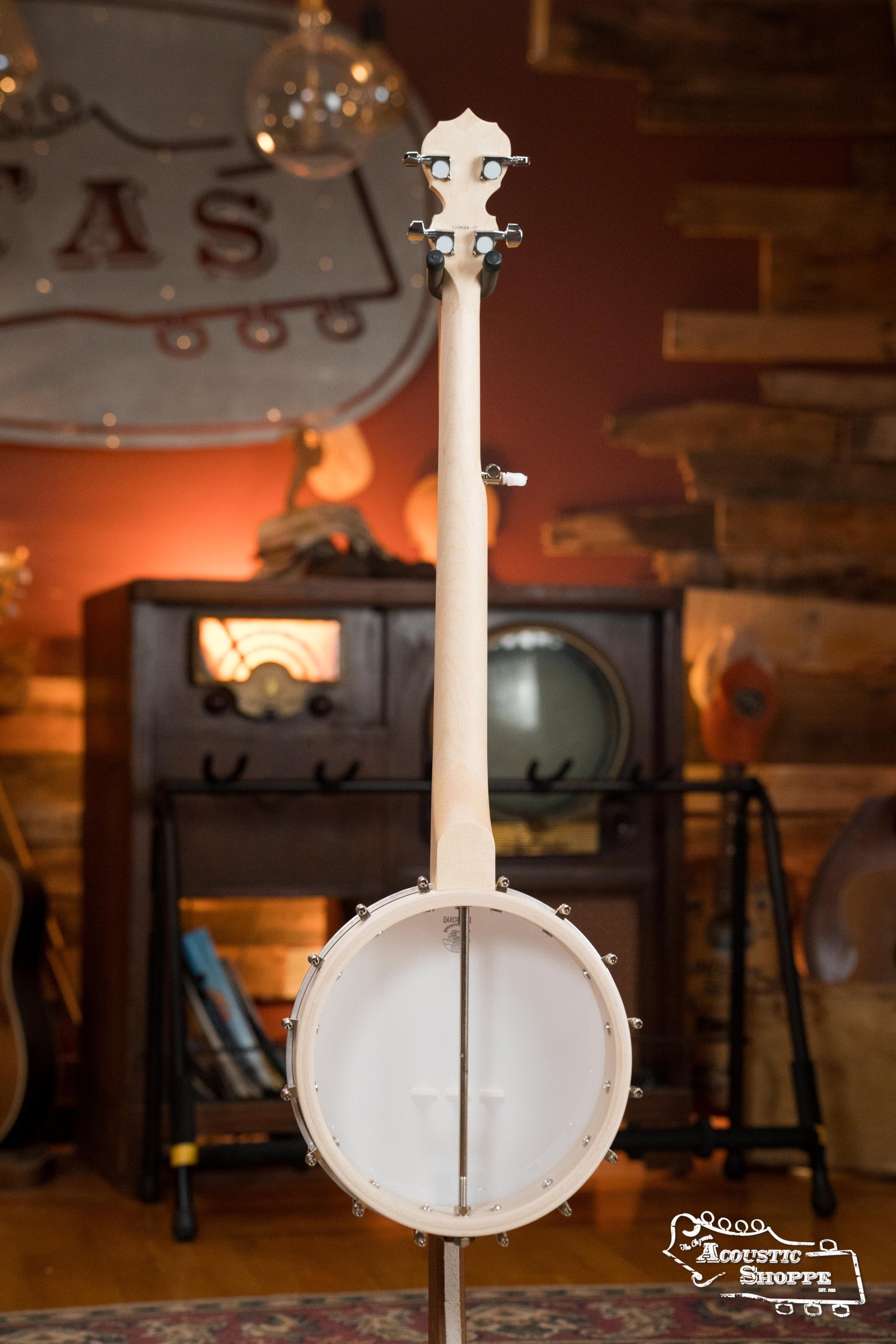 The Deering Banjos Goodtime Deco 5-String Banjo #62407 is displayed upright from the back in a cozy, rustic room with wood paneling, vintage decor, an old radio, and other musical instruments in the background.