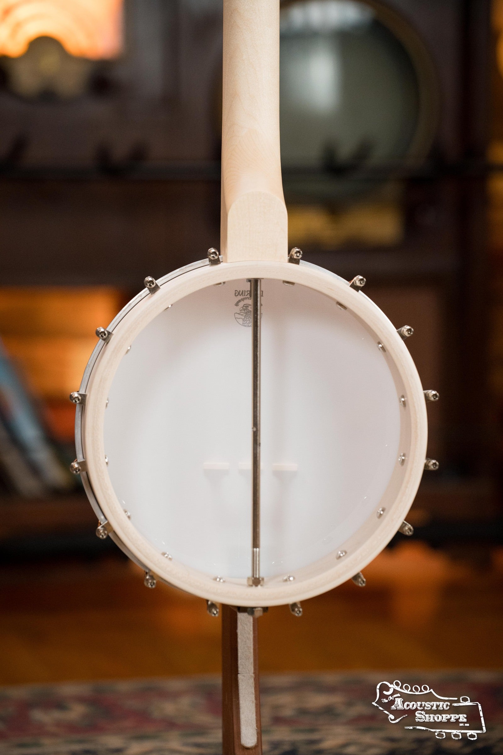 Close-up of the back of a Deering Banjos Goodtime Deco 5-String Banjo #62407 showing its light wood frame and white drumhead, shot indoors with a blurred background. The Acoustic Shoppe logo appears in the bottom right corner.