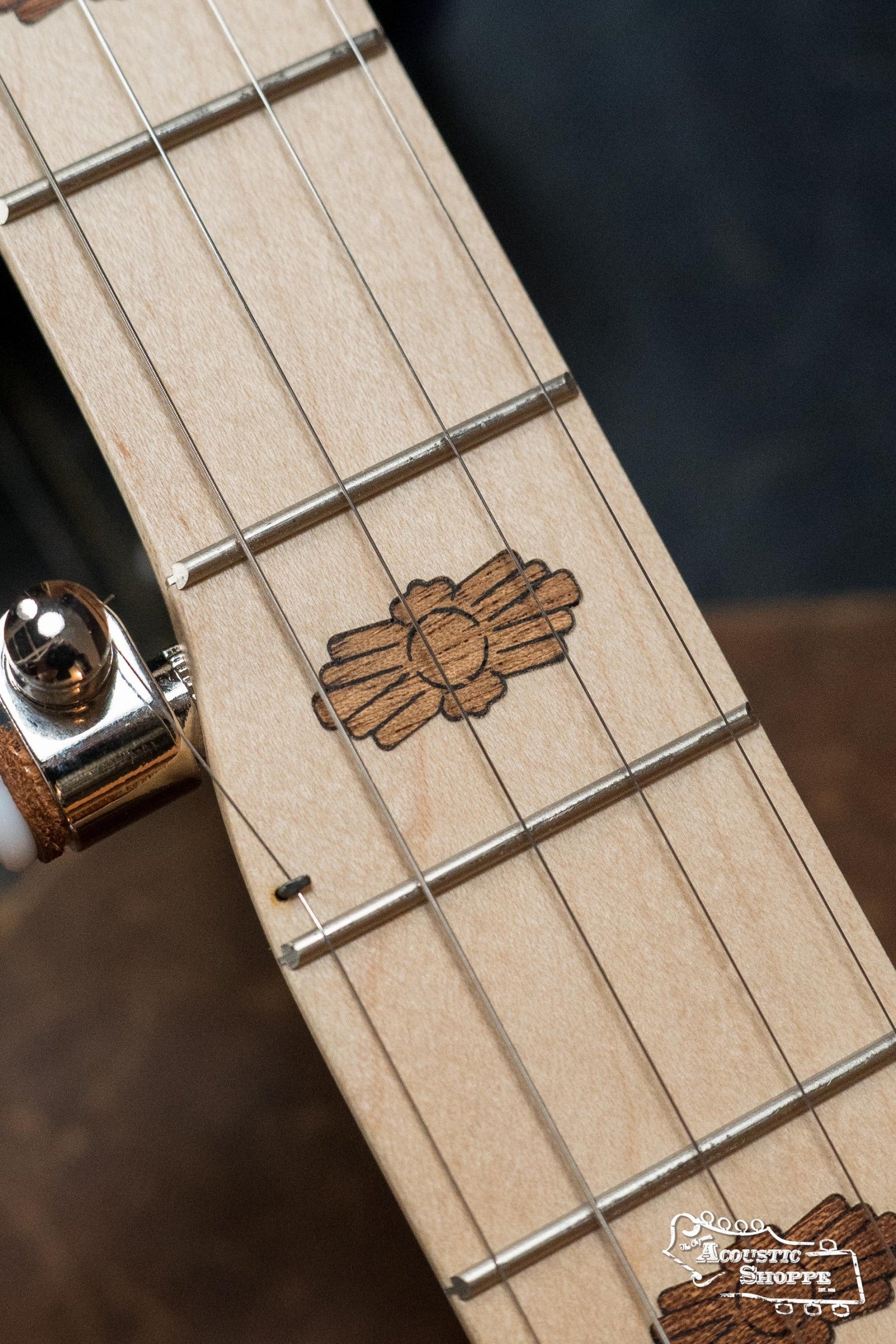 Close-up of the Deering Goodtime Deco 5-String Banjo #62407 by Deering Banjos, showing its metal frets and Art Deco-style thunderbird wood inlay. The tuning peg and part of the banjo body are also partially visible.