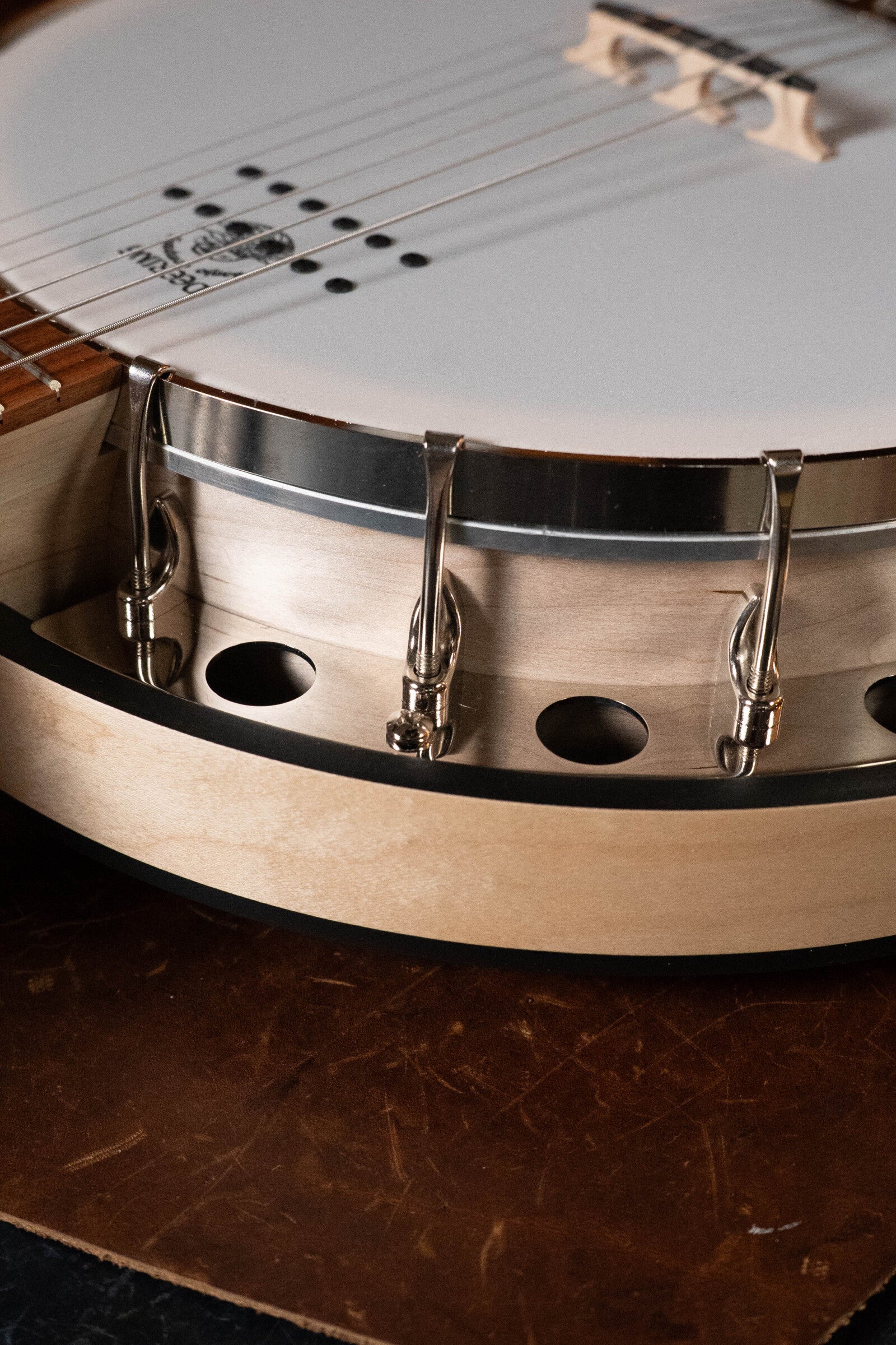 Close-up of a Deering Banjos Goodtime Six-R 6-String Resonator Banjo with Kavanjo Pickup (#2520), highlighting its strings, bridge, metal hooks, and circular wooden body with sound holes against a brown surface.
