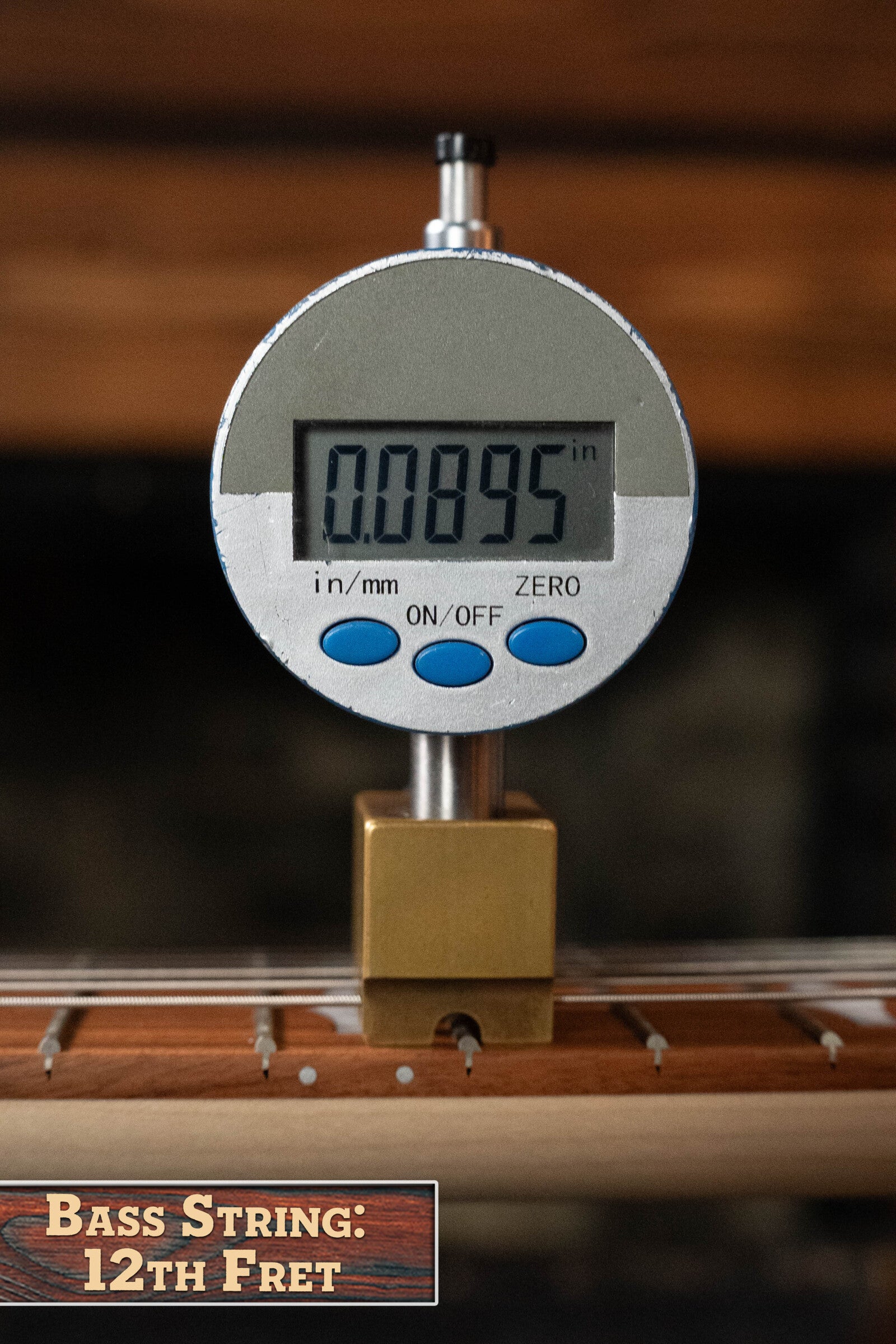 A digital gauge displays 0.0895 inches at the 12th fret of a Deering Goodtime Six-R 6-String Resonator Banjo w/Kavanjo Pickup by Deering Banjos. A small sign reads, “Bass String: 12th Fret.”.