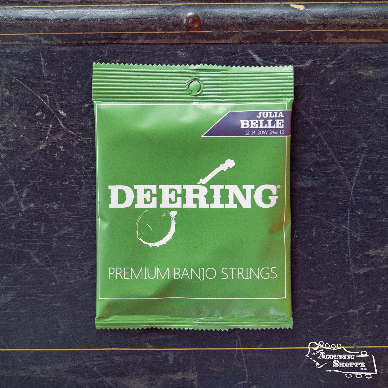A green packet of Deering Julia Belle 5 String Banjo Strings by Deering Banjos, featuring a banjo graphic and The Acoustic Shoppe logo, lies on a dark surface—ideal strings (12 14 20W 24W 12) for low tuning setups.