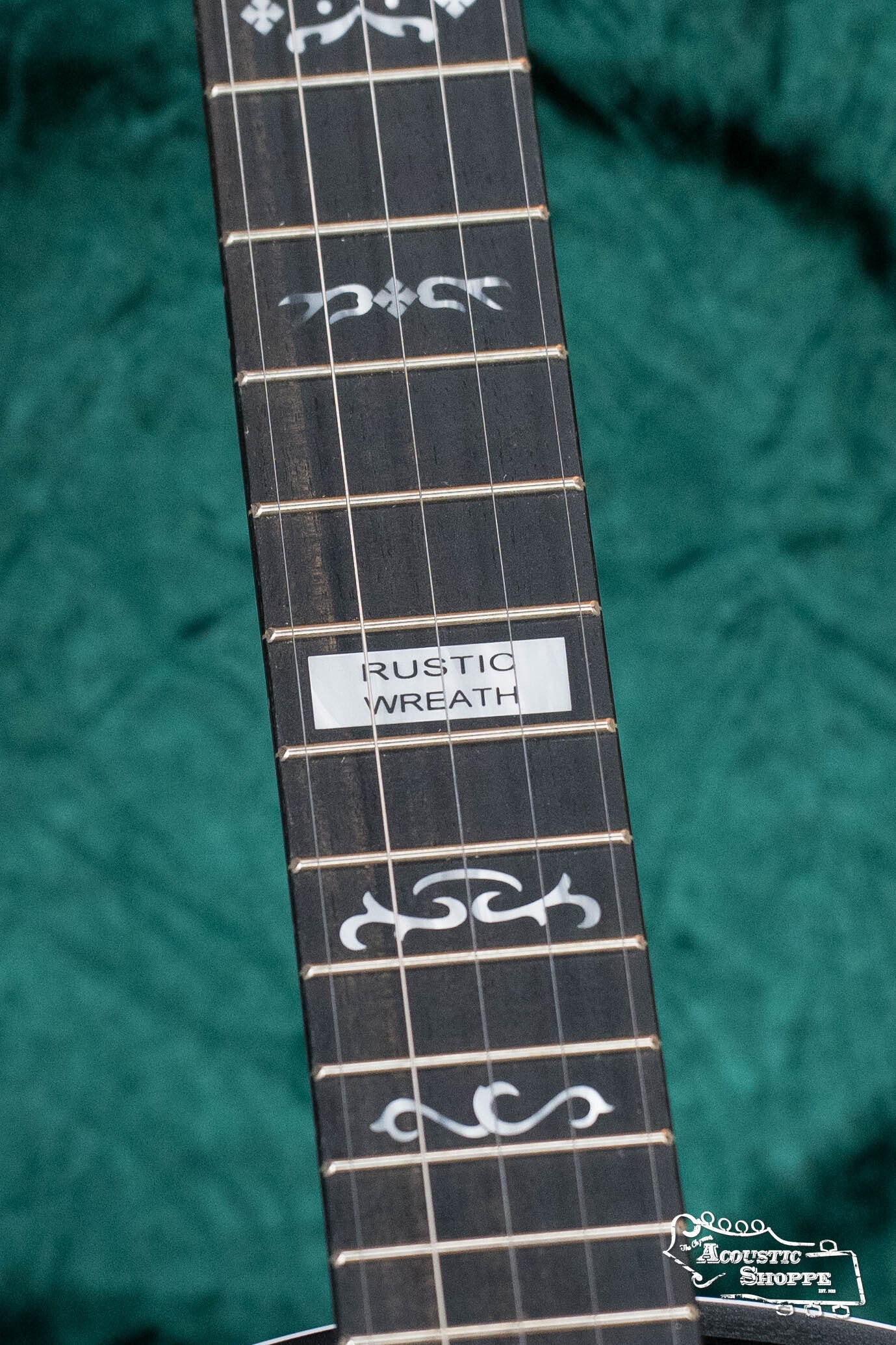 Close-up of a Deering Banjos Rustic Wreath 5-String Resonator Banjo #AU45 neck shows decorative fretboard inlays and a label, set against dark green fabric for a classic look.