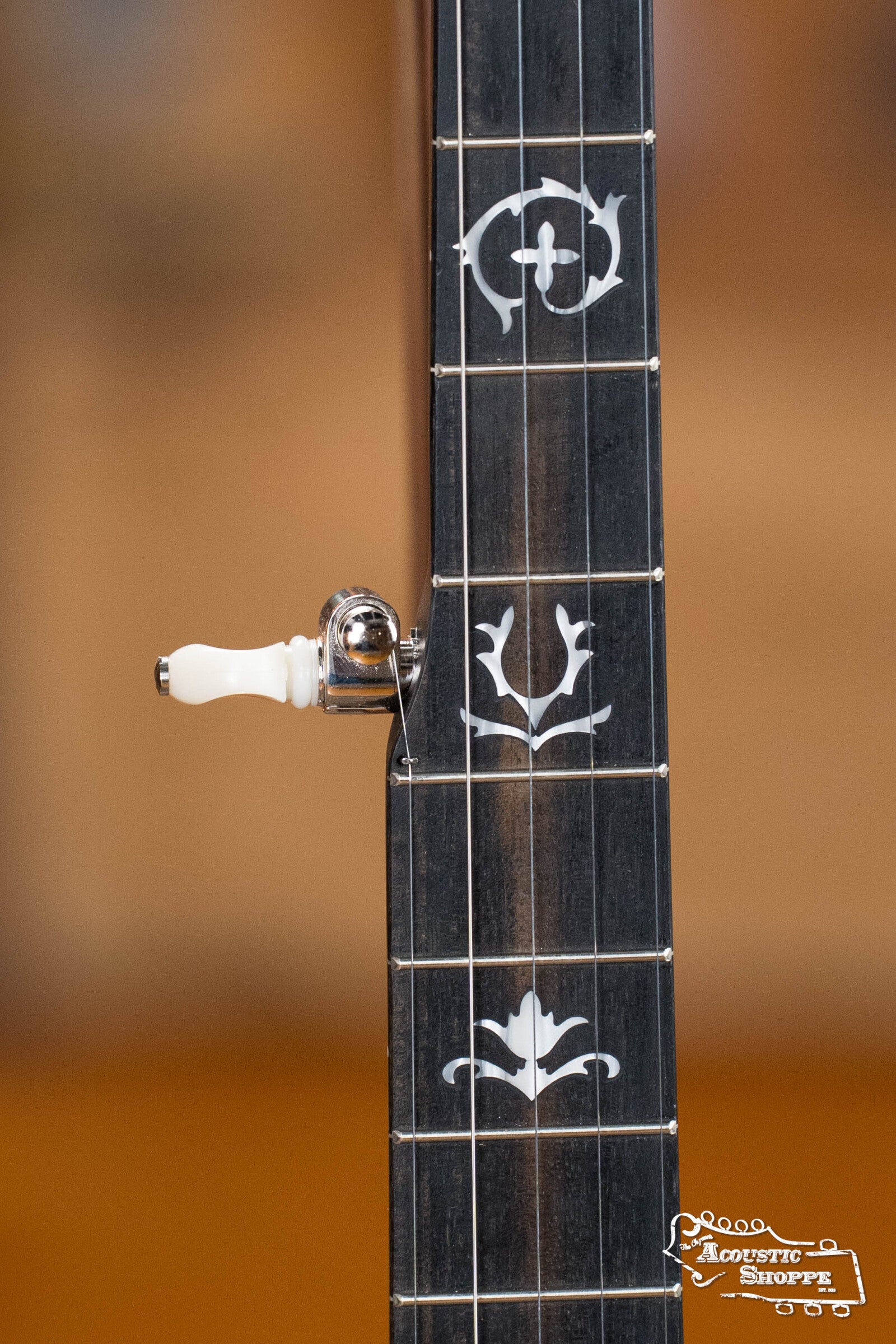 Close-up of a Deering Rustic Wreath 5-String Resonator Banjo #AU45 by Deering Banjos shows detailed white fretboard inlays and a tuning peg. The blurred background features the Acoustic Shoppe logo, ideal for bluegrass banjo fans.