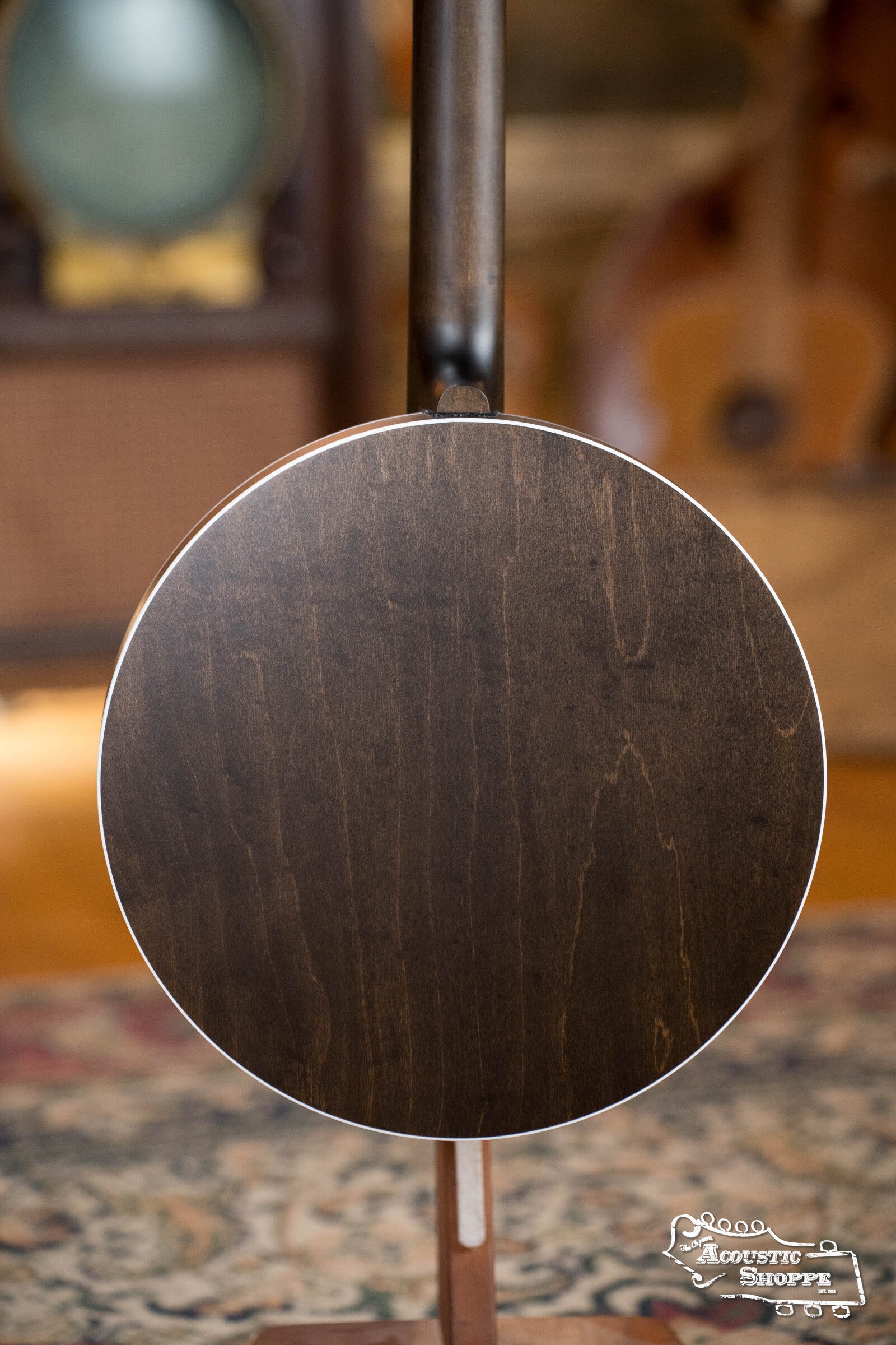 The image shows the back of a Deering Rustic Wreath 5-String Resonator Banjo #AU45 by Deering Banjos on a stand, set against a blurred vintage background and patterned rug. The Acoustic Shoppe logo appears in the bottom right corner.