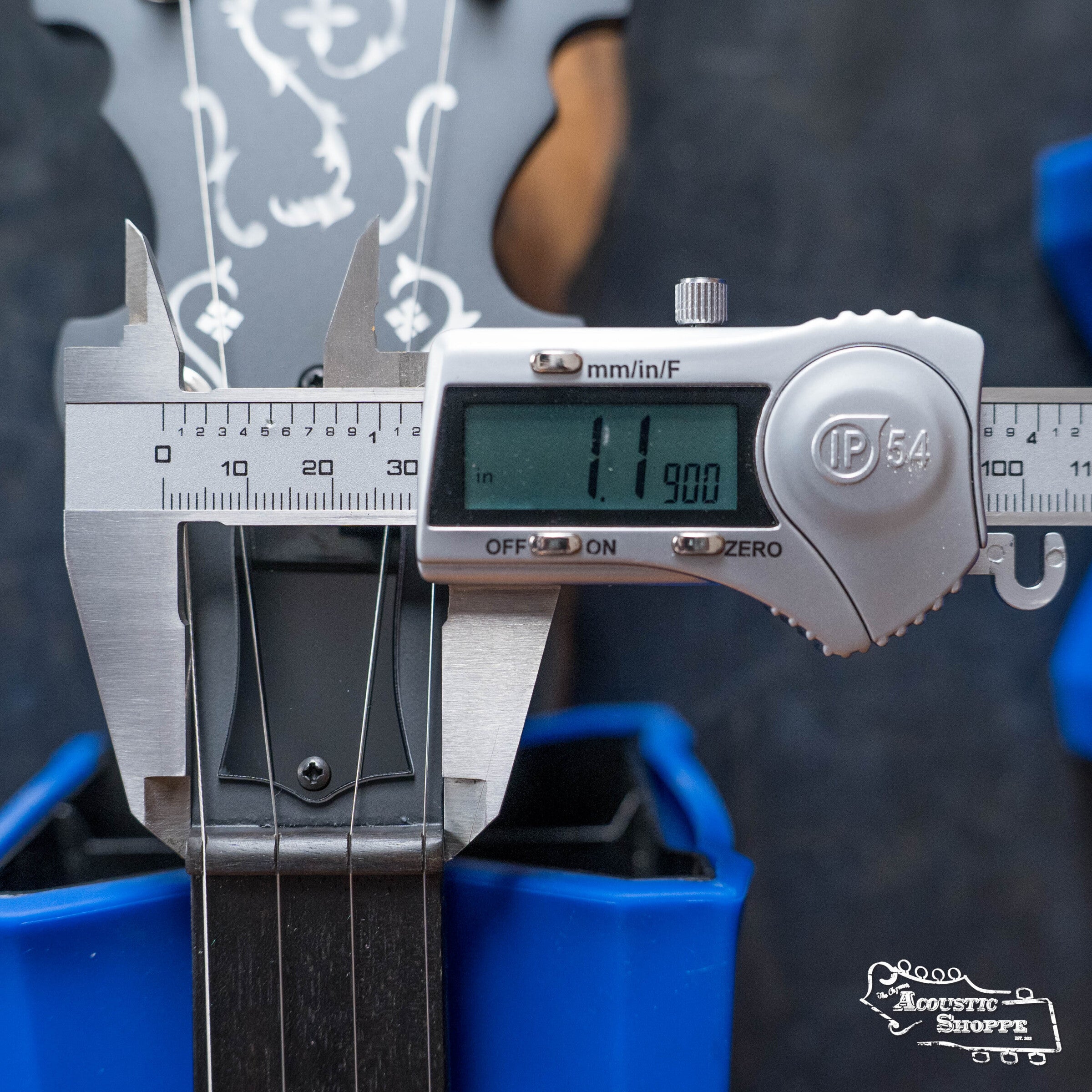 A digital caliper measures a guitar neck at 11.90 mm, with the fretboard in view and the headstock of a Deering Rustic Wreath 5-String Resonator Banjo #AU45 by Deering Banjos partially visible in the background.