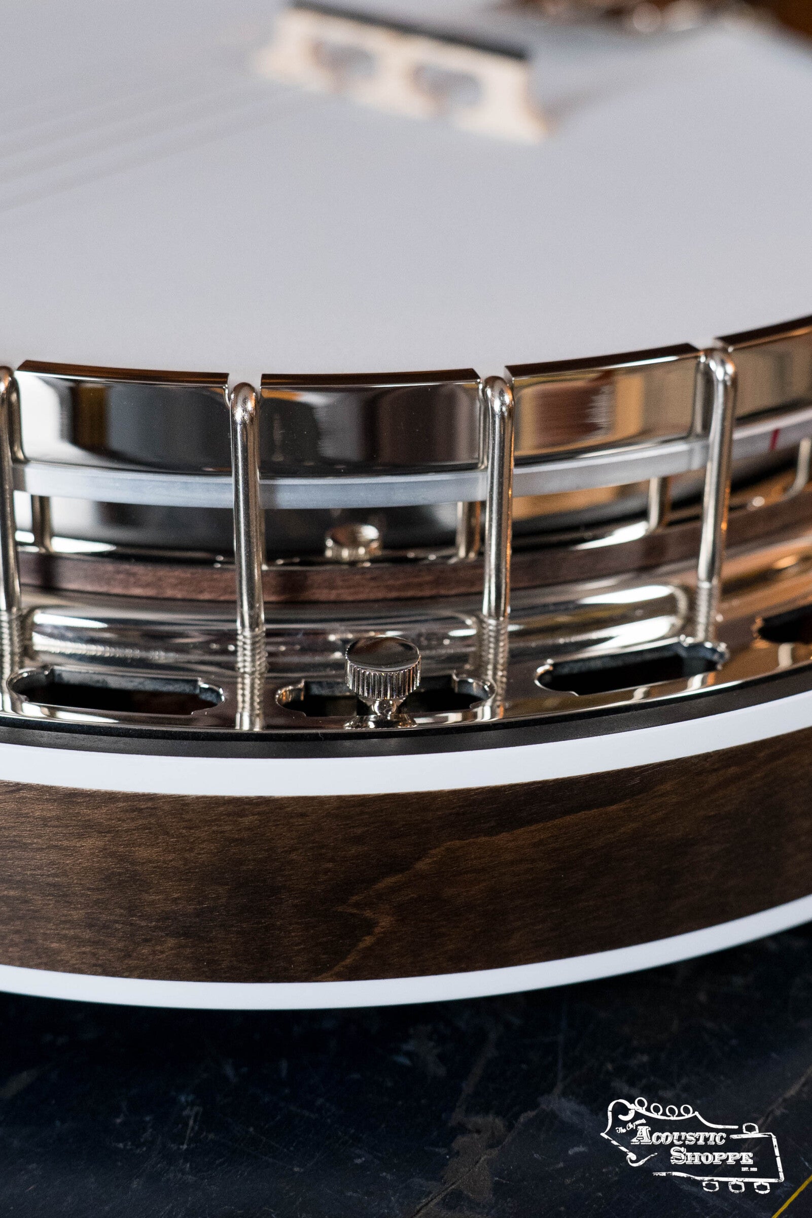 Close-up of a Deering Rustic Wreath 5-String Resonator Banjo #AU45 by Deering Banjos, showing its wooden rim, metal hardware, and white drumhead on a dark surface with the Acoustic Shoppe logo—true bluegrass banjo appeal.