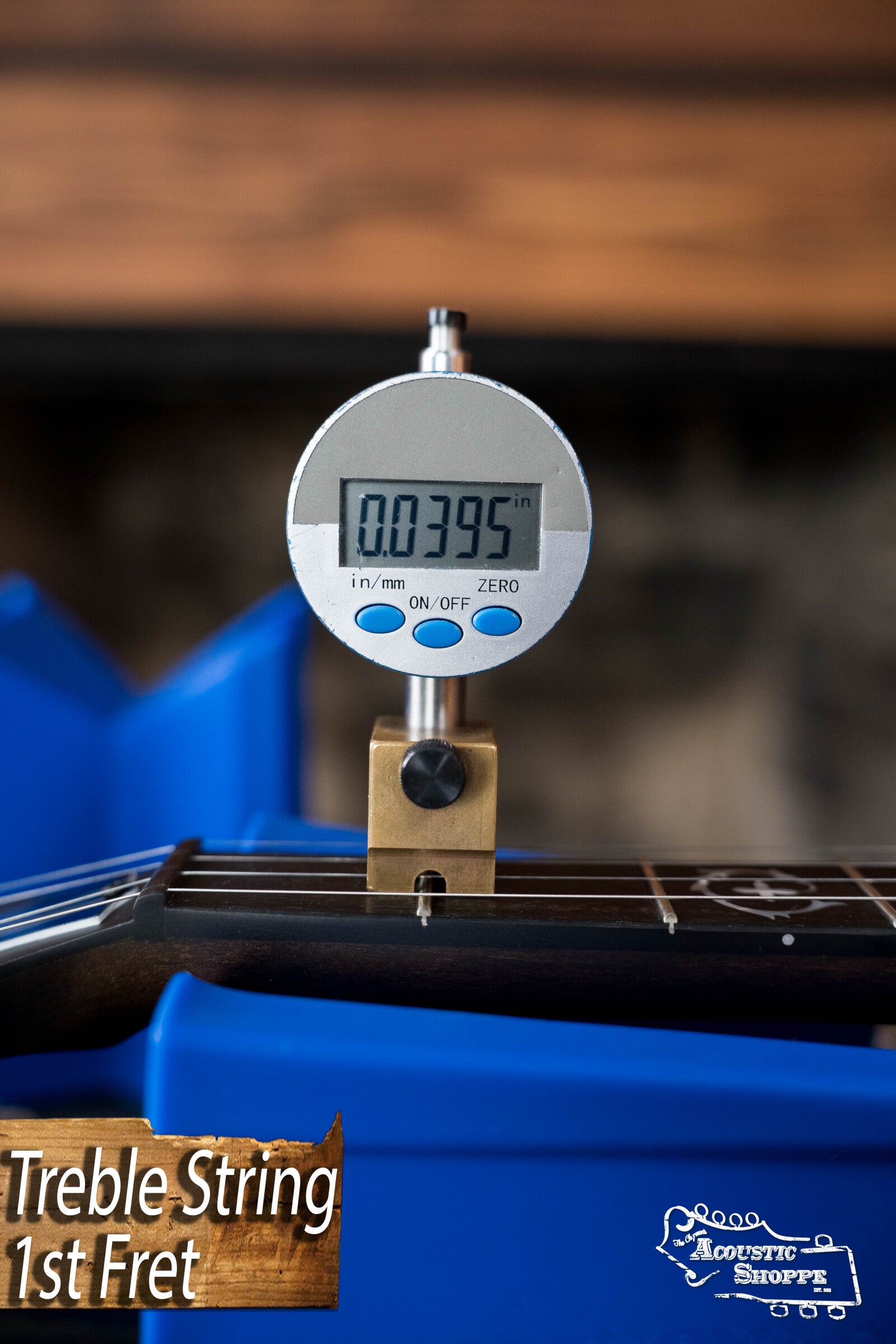 A digital gauge reads 0.0395 inches at the 1st fret of a Deering Rustic Wreath 5-String Resonator Banjo #AU45 by Deering Banjos, resting in a blue holder with an Acoustic Shoppe logo and label below.