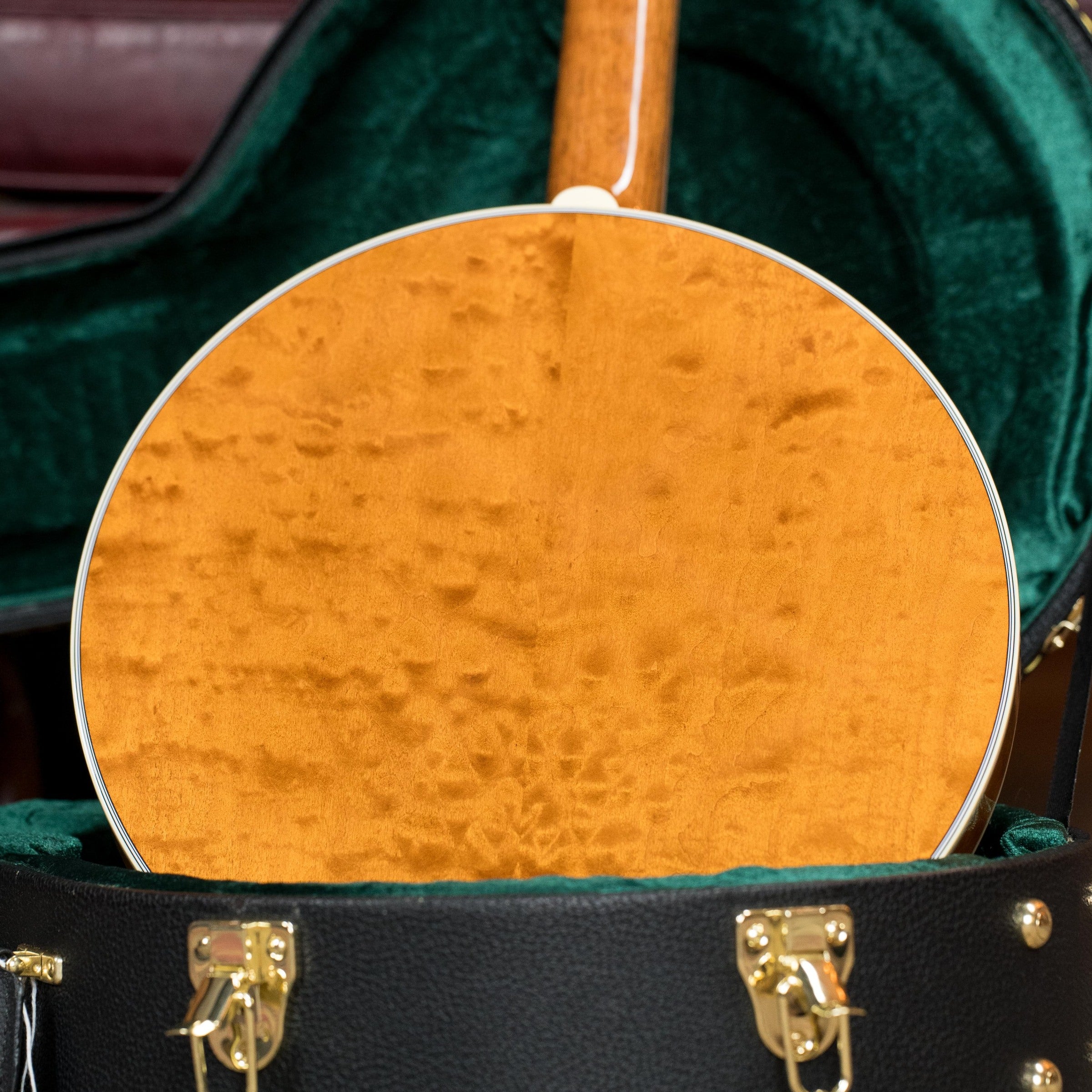 A close-up of the Deering Banjos Tony Trischka Silver Clipper Resonator Banjo w/Spikes at 7, 8, 9, and 10 #0100 shows its golden figured wood back in a green velvet-lined black case with gold latches—ideal for bluegrass fans.