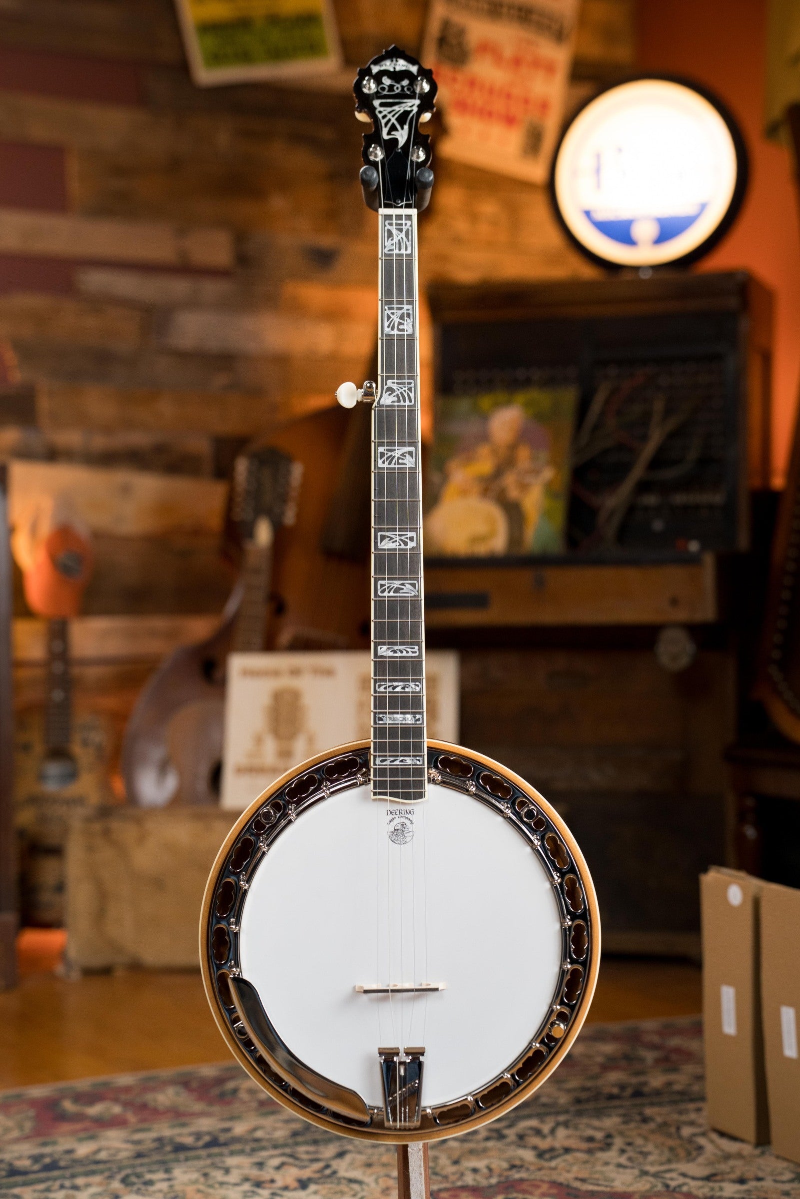A Deering Banjos Tony Trischka Silver Clipper Resonator Banjo w/Spikes Installed at 7, 8, 9, and 10 (#0100) stands upright on a patterned rug in a rustic wooden room, evoking bluegrass spirit among other musical instruments.